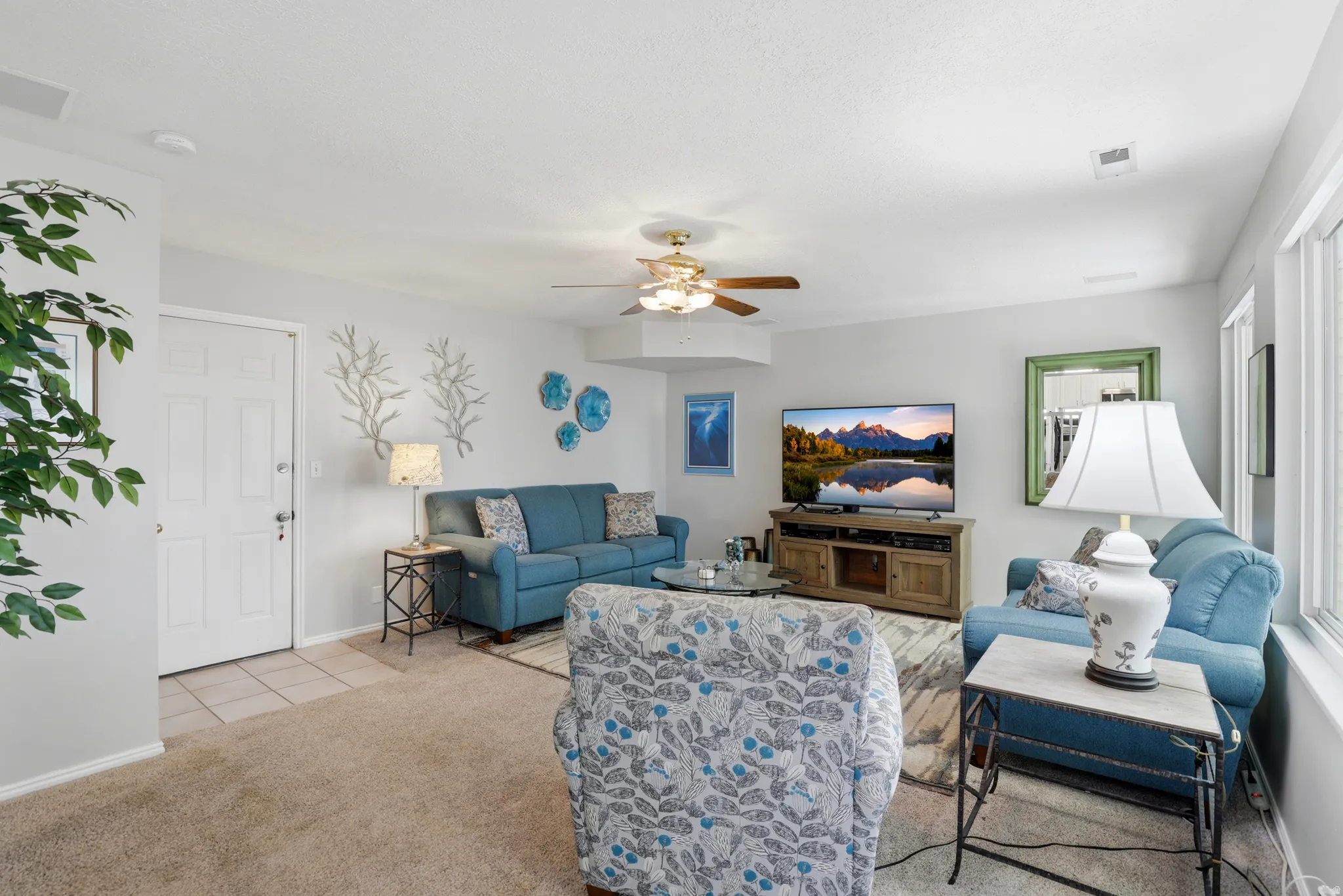 Bright living area featuring light neutral wall paint, carpet flooring, a ceiling fan, and multiple windows