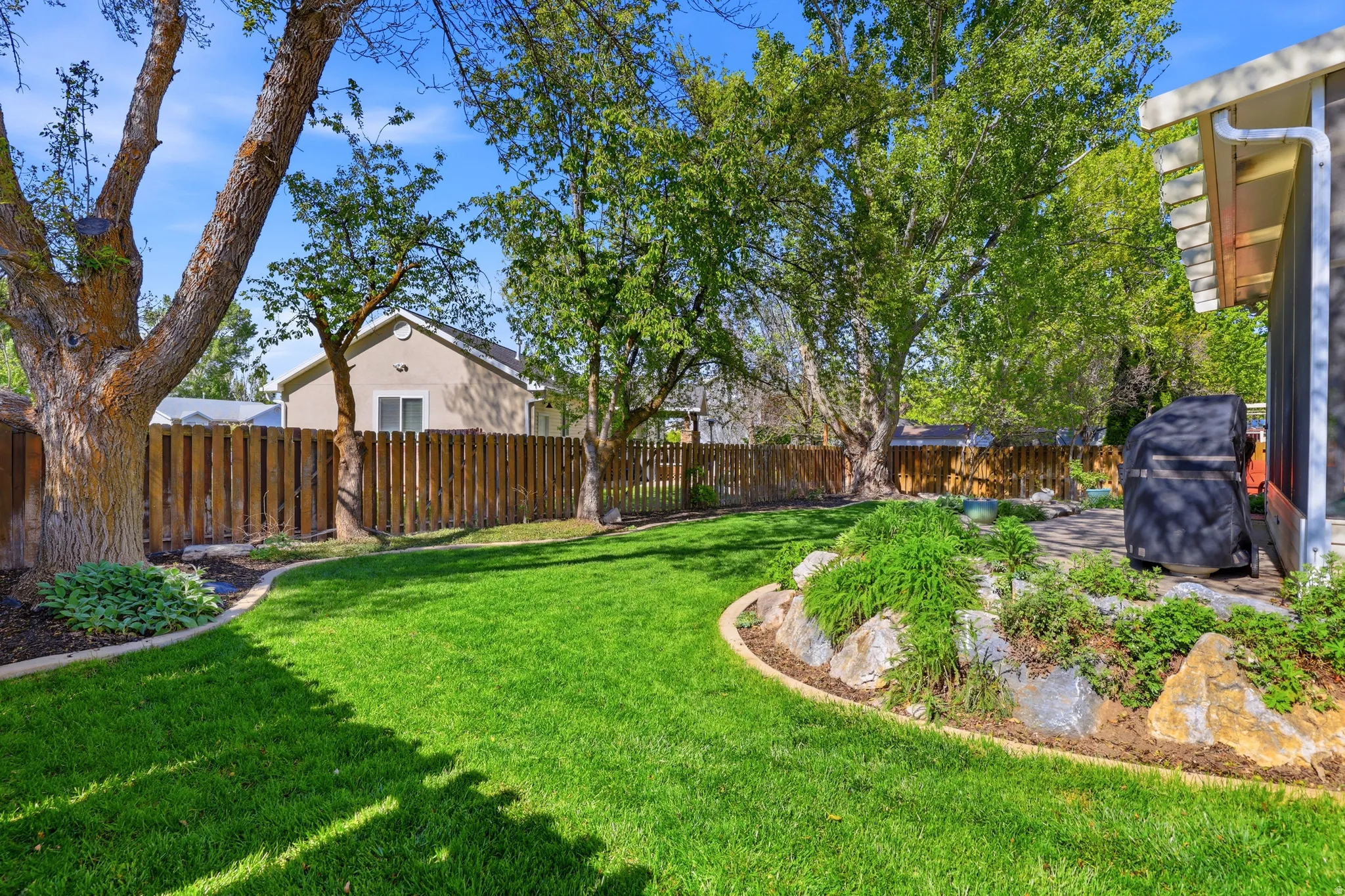 Spacious backyard featuring a manicured lawn, established shade trees, and a wooden privacy fence