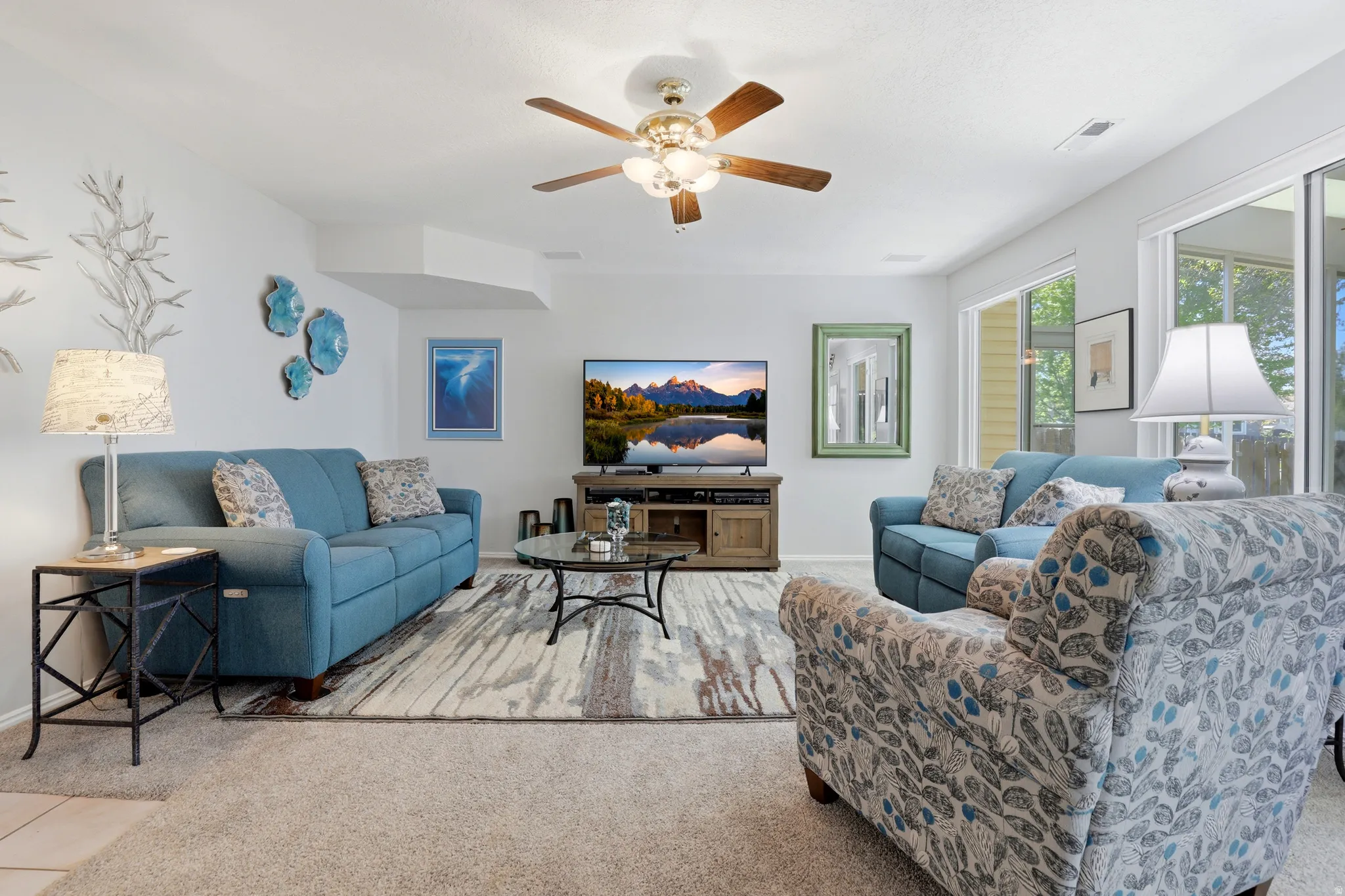 Spacious living area featuring a ceiling fan, a mix of carpet and wood-finish flooring, and large sliding glass doors providing ample natural light