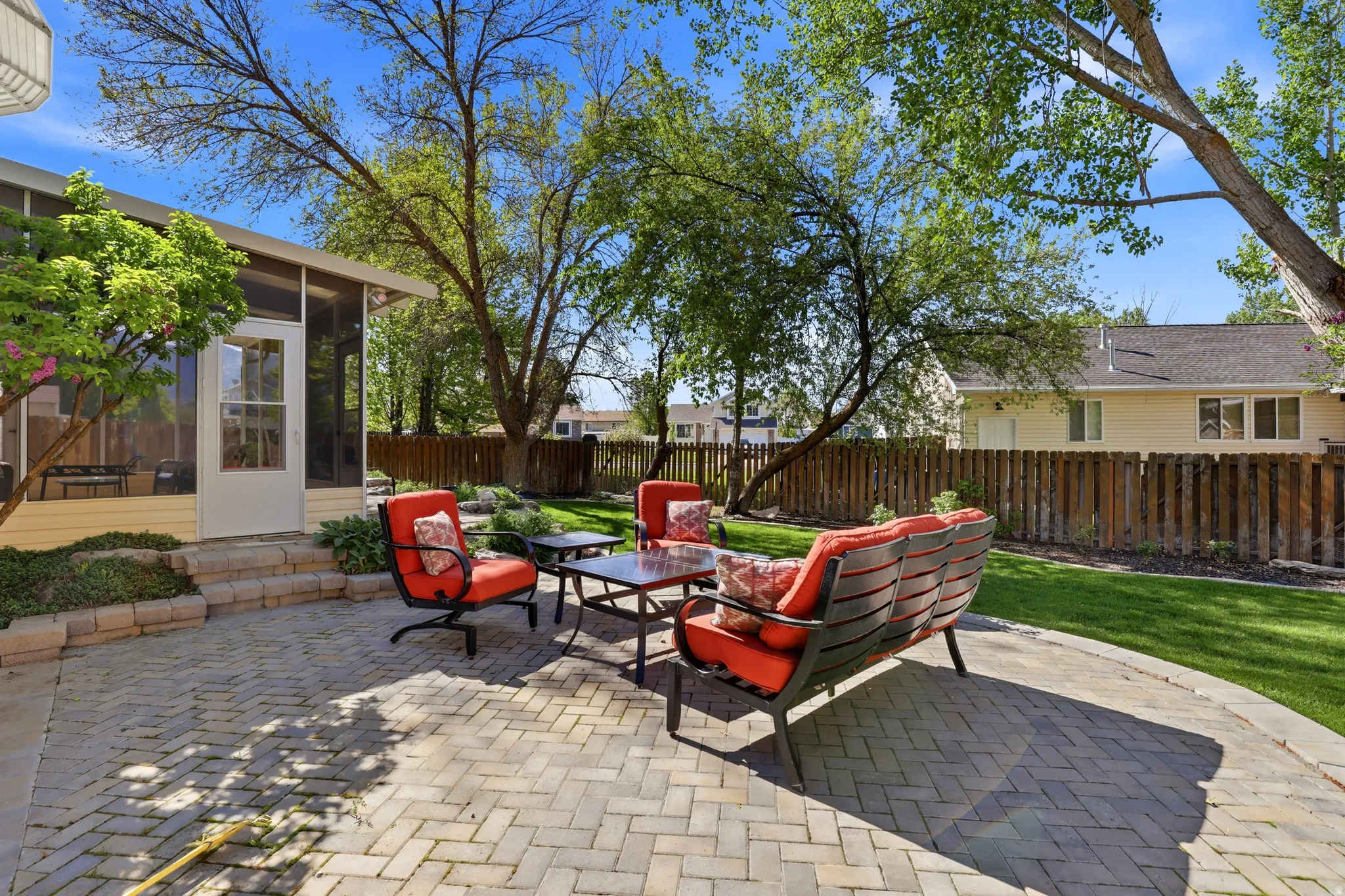 Paved patio featuring a herringbone pattern, bordered by a manicured lawn and mature trees