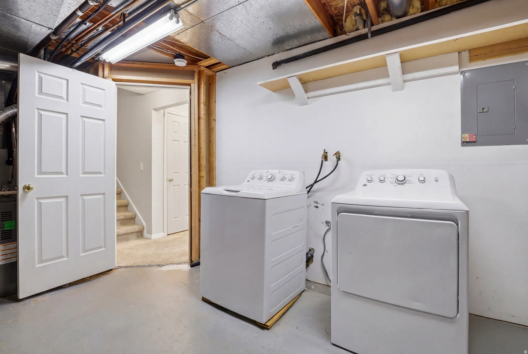 Dedicated laundry area featuring a washer and dryer, painted concrete flooring, and exposed ceiling joists