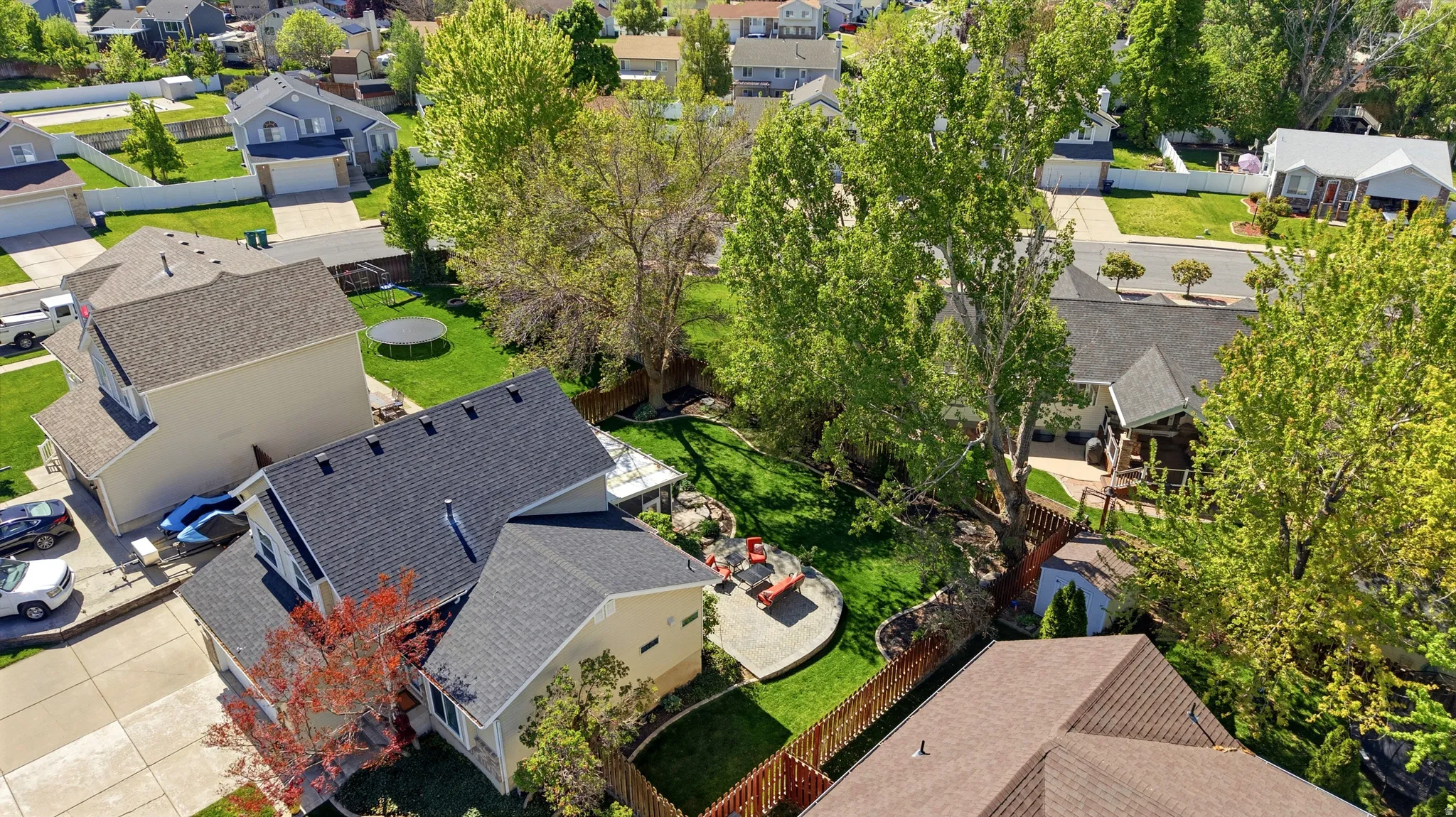 Expansive backyard featuring a manicured lawn, established shade trees, and a circular paved patio