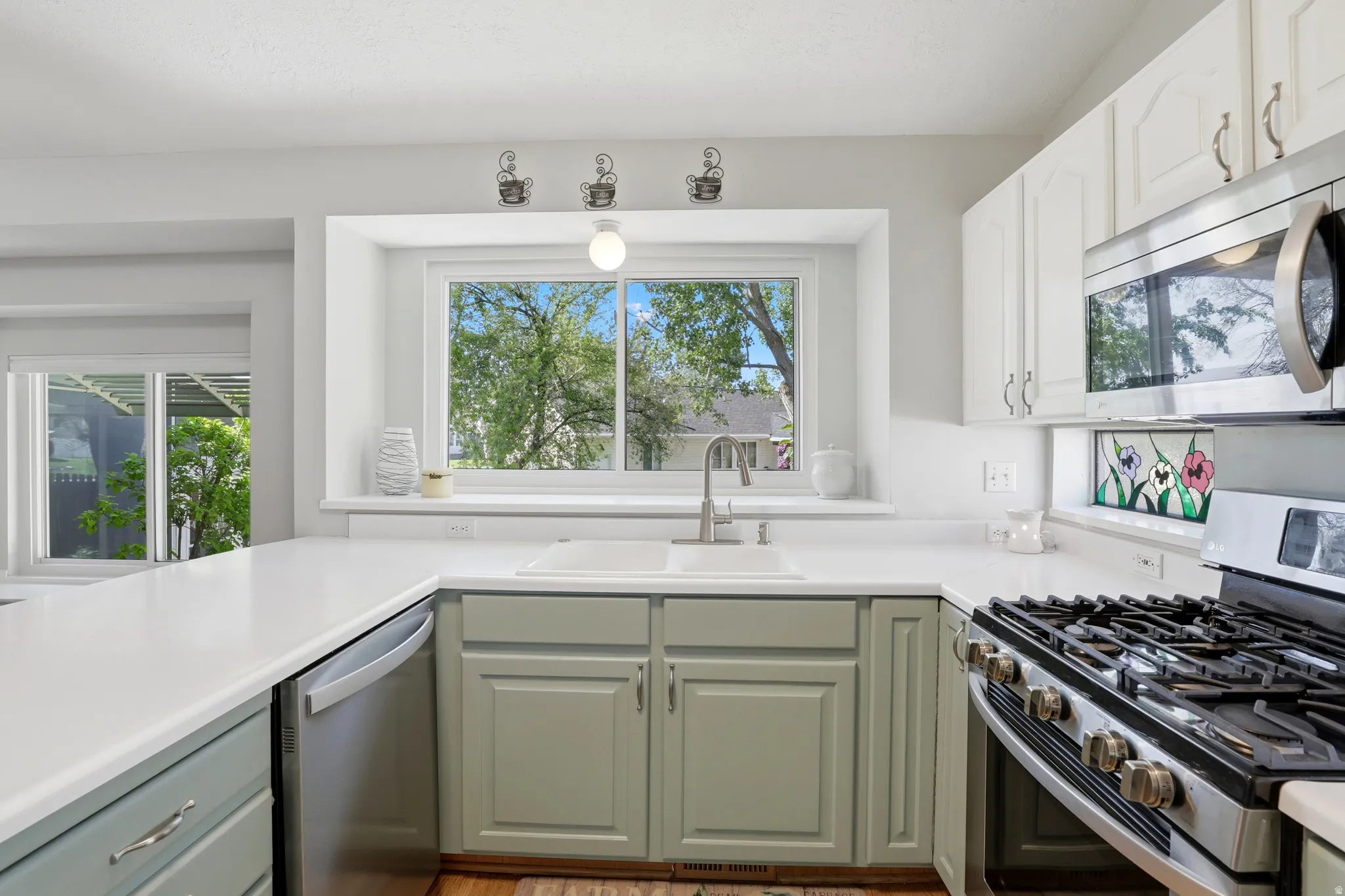 Kitchen featuring light-colored countertops, a built-in stainless steel microwave, a gas range with a stainless steel finish, white upper cabinetry, and a double-basin sink