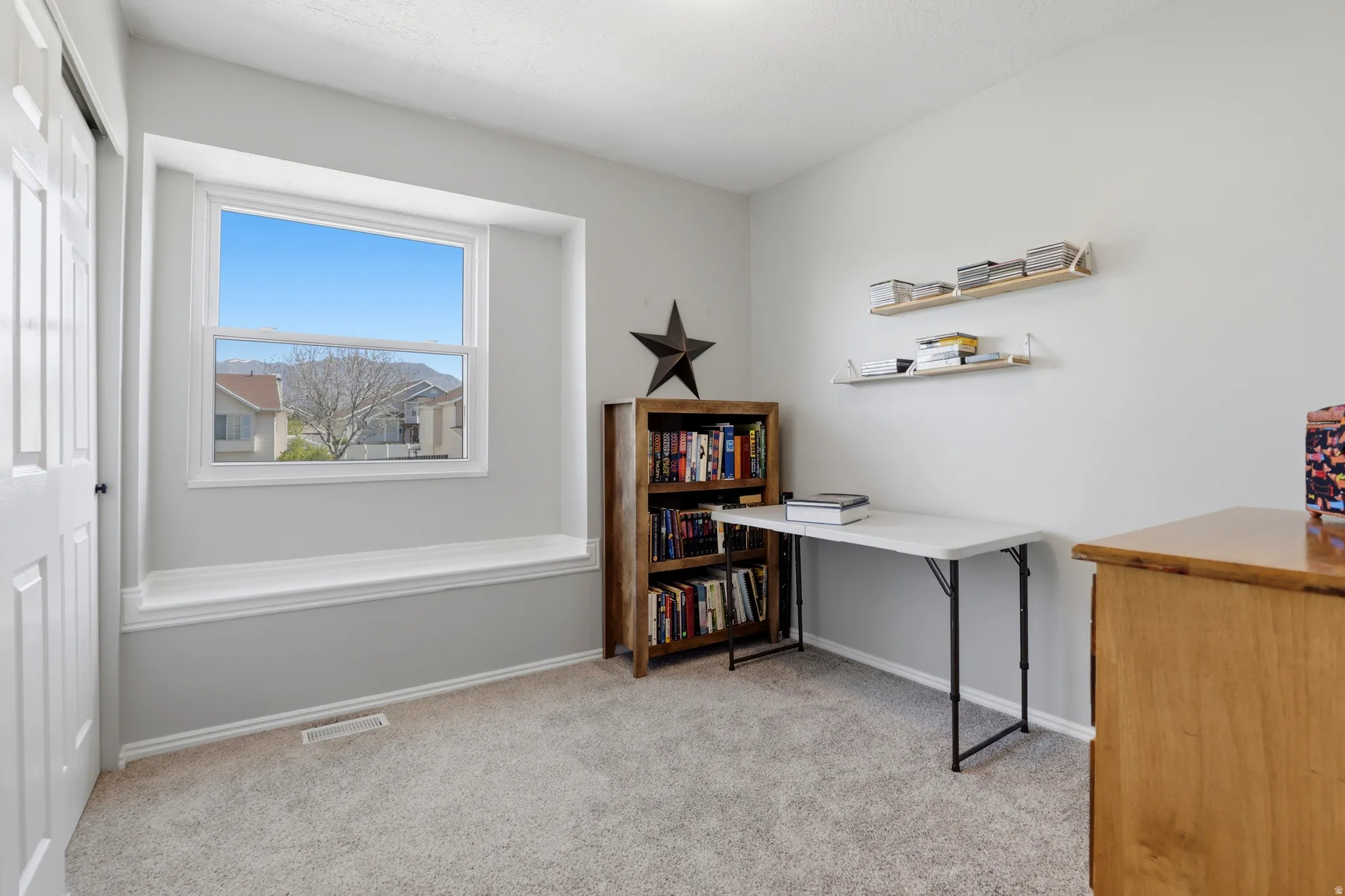Bright room featuring a wide window with a built-in window bench, light gray walls, plush gray carpeting, and white trim