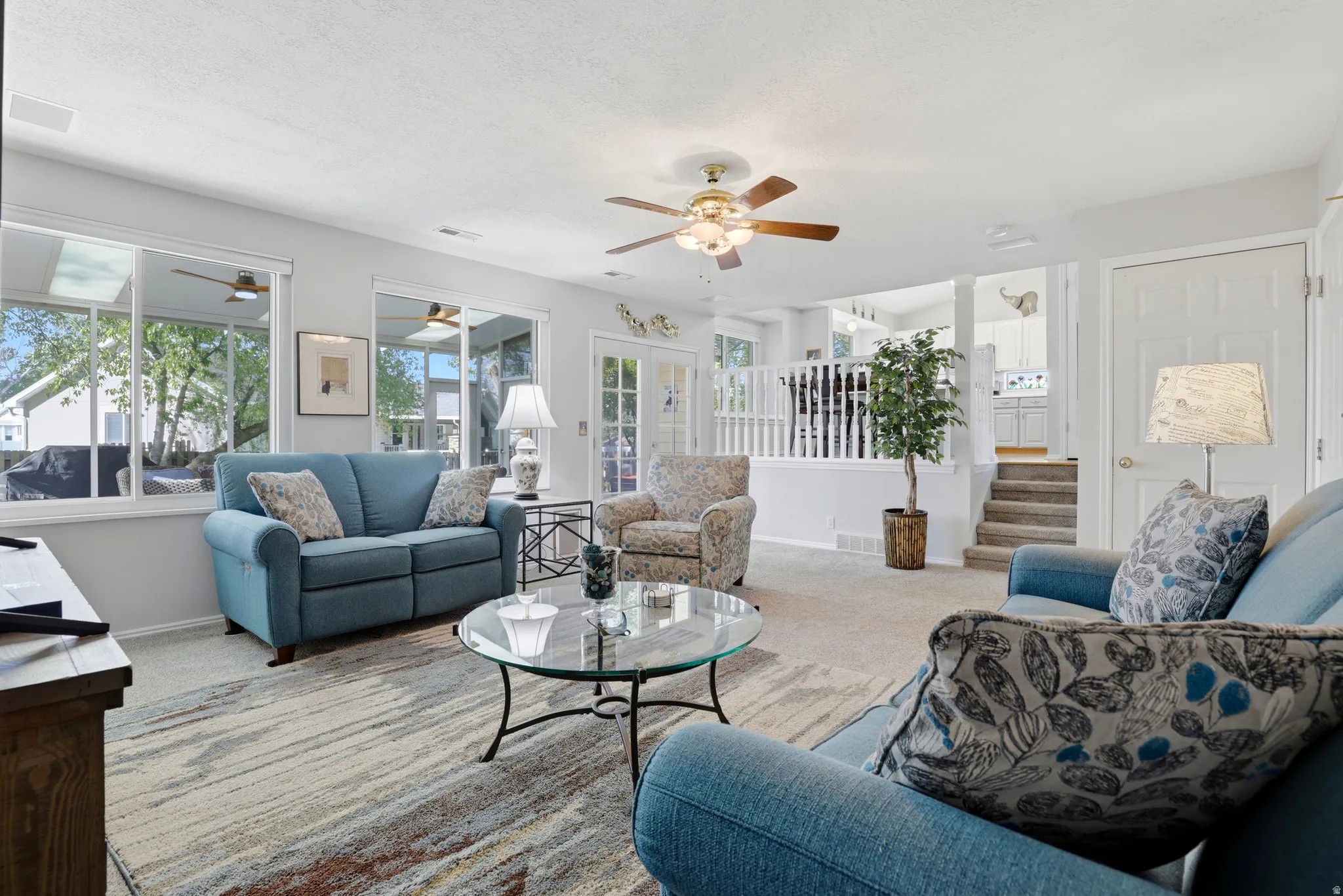 Spacious living area featuring light-colored carpeting, multiple windows, and a ceiling fan
