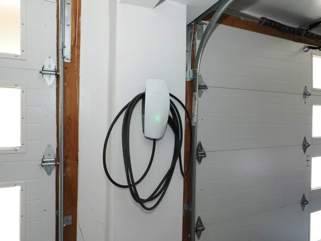 Dedicated electric vehicle charging station mounted on a wall within the garage