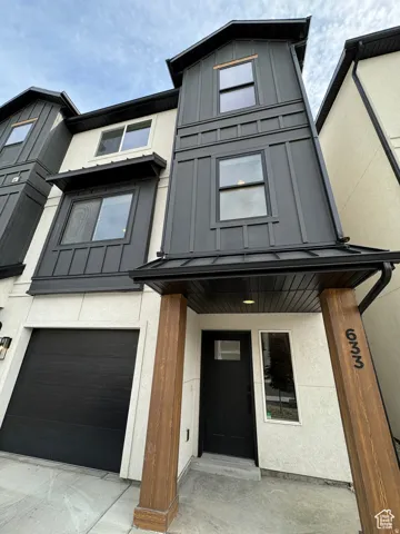 View of front of home featuring an attached garage, covered porch, stucco siding, and board and batten siding