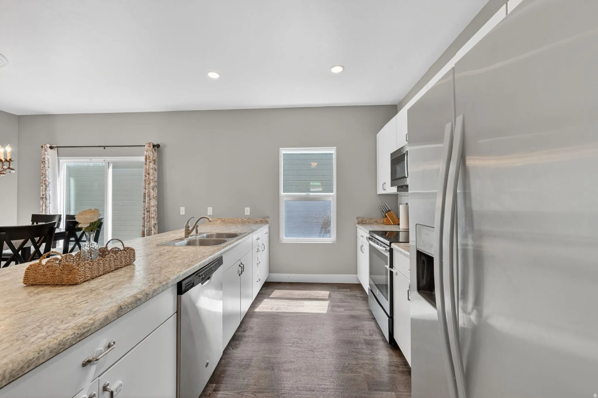 Kitchen featuring an expansive island with dual sinks, white cabinetry, stainless steel appliances, wood-finish flooring, and a sliding glass door