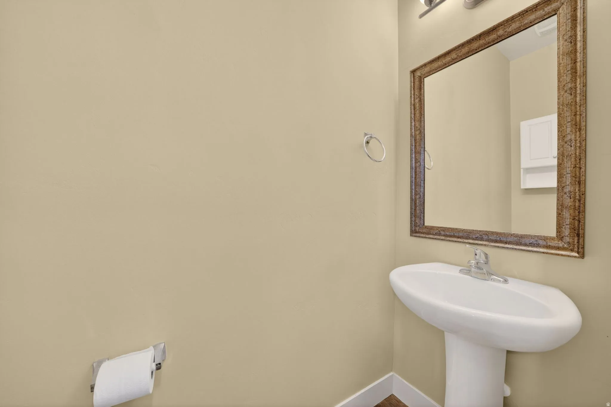Pedestal sink with a chrome faucet, ornate framed mirror, and warm beige wall tones