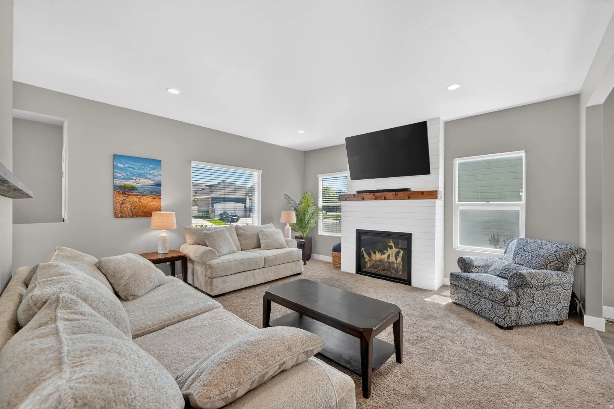 Spacious living area featuring a white brick fireplace with a wood mantle, recessed lighting, multiple windows, and light gray wall tones