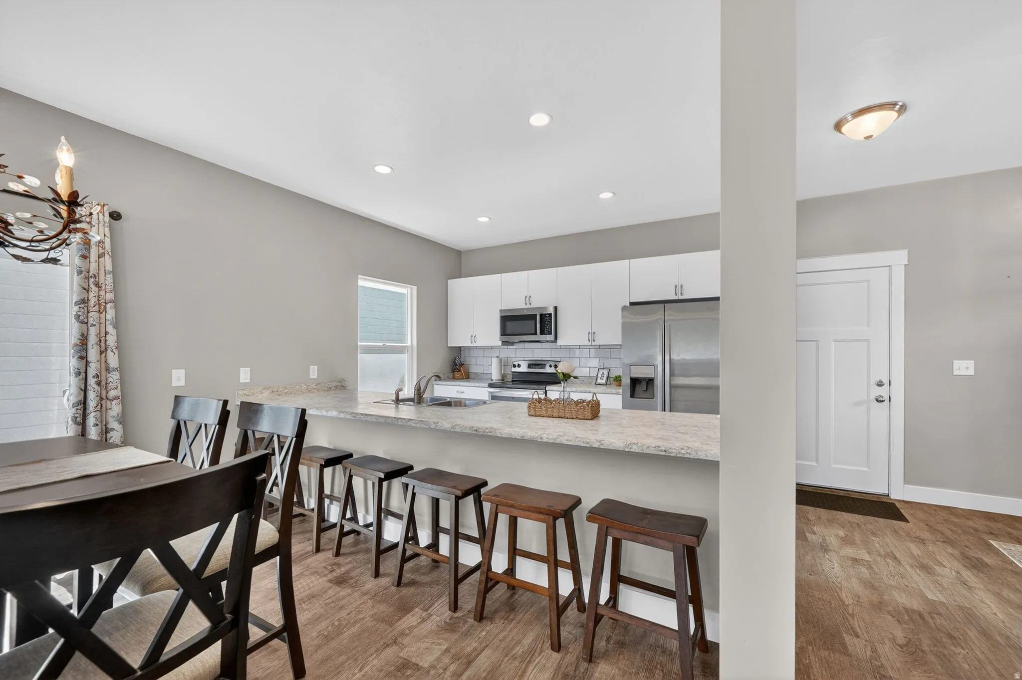 Bright kitchen featuring white cabinetry, stainless steel appliances, a white subway tile backsplash, and a breakfast bar with seating