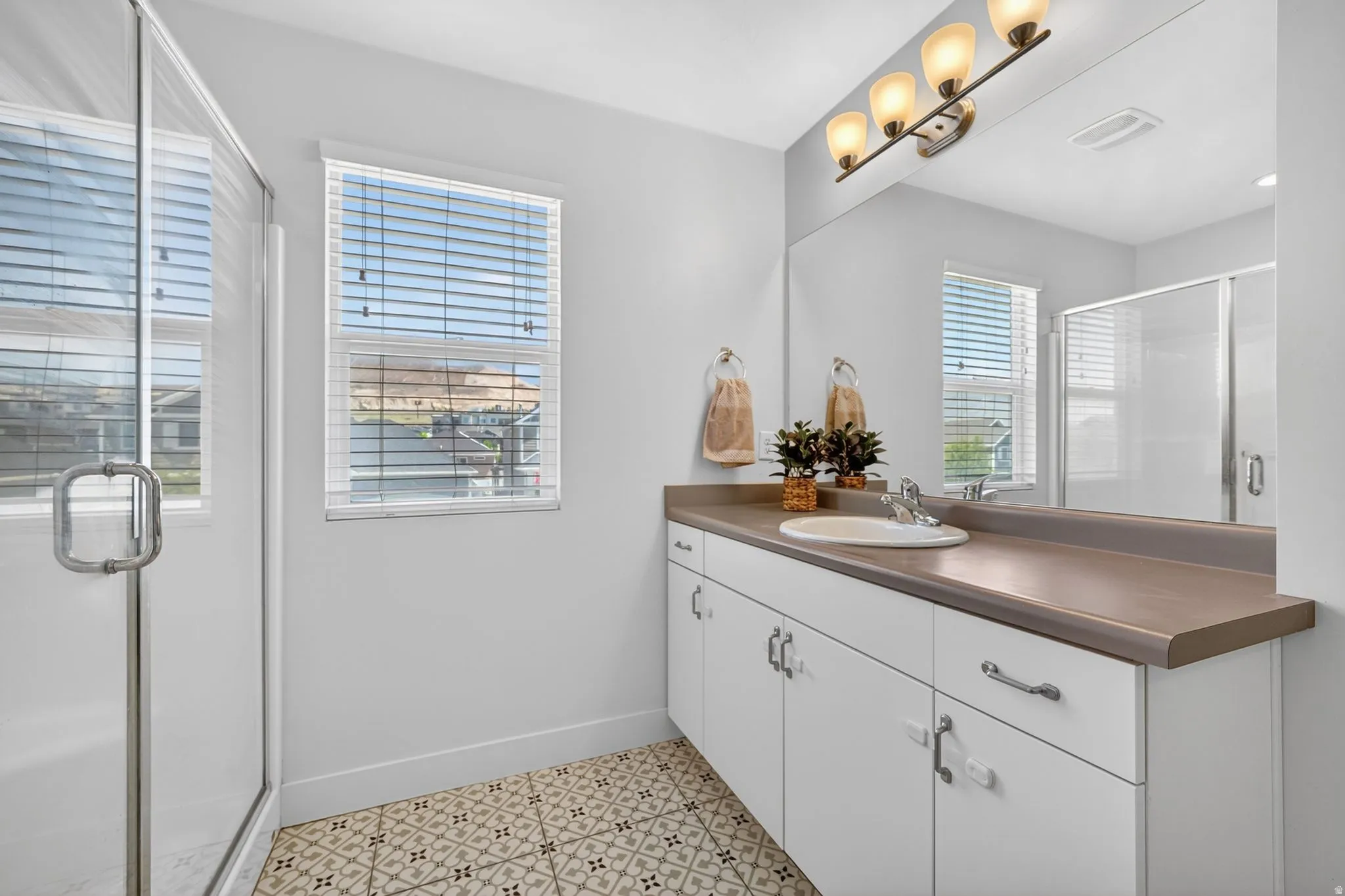 White vanity with a single basin sink and a neutral countertop, large mirror, and four-light fixture