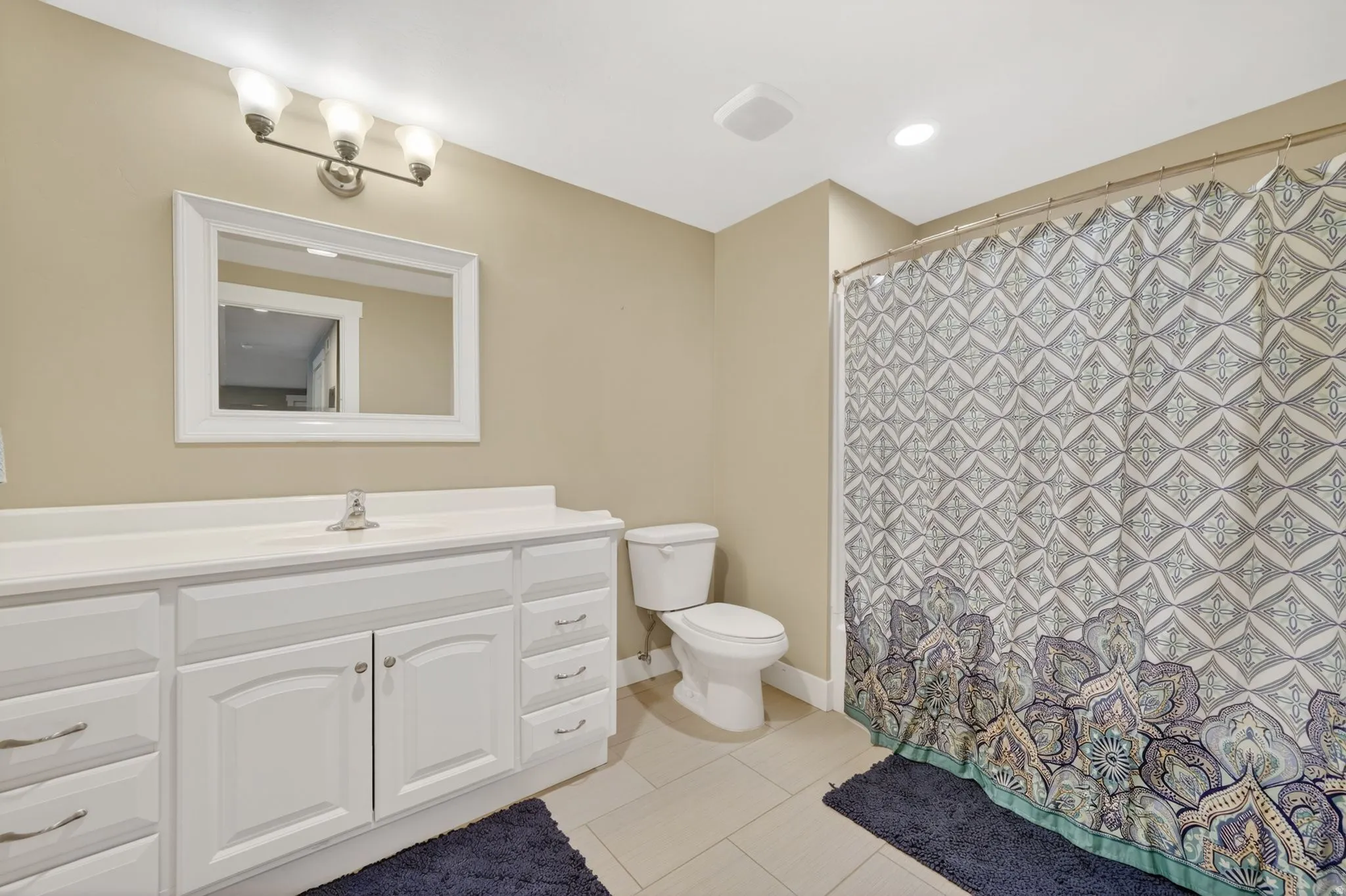 Full bathroom featuring a white vanity with extensive storage, a white framed mirror, and a three-light fixture