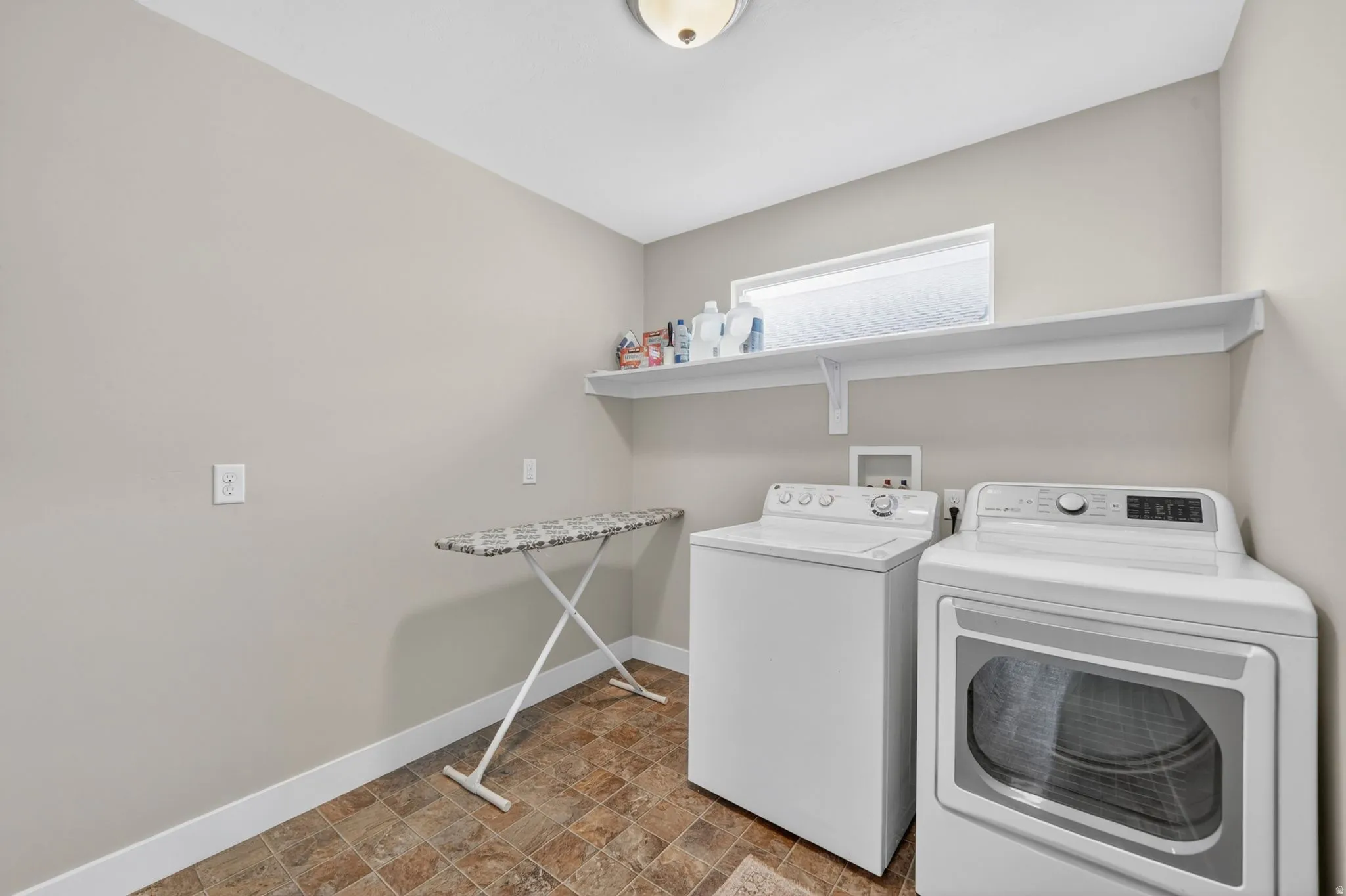 Dedicated laundry room featuring durable tile flooring, a horizontal window, and an overhead storage shelf
