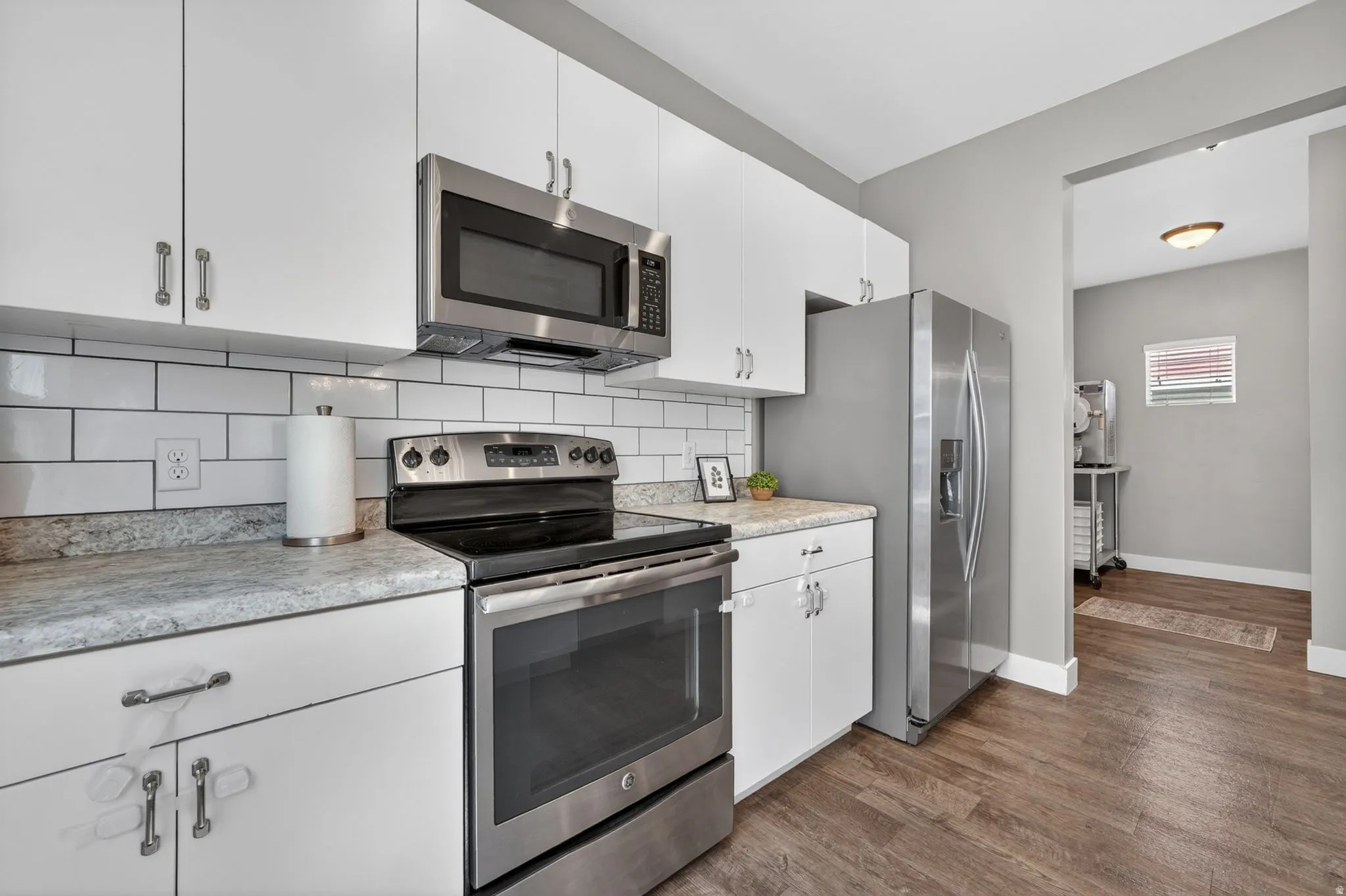 Kitchen featuring white cabinetry, subway tile backsplash, stainless steel appliances, and wood-finish flooring