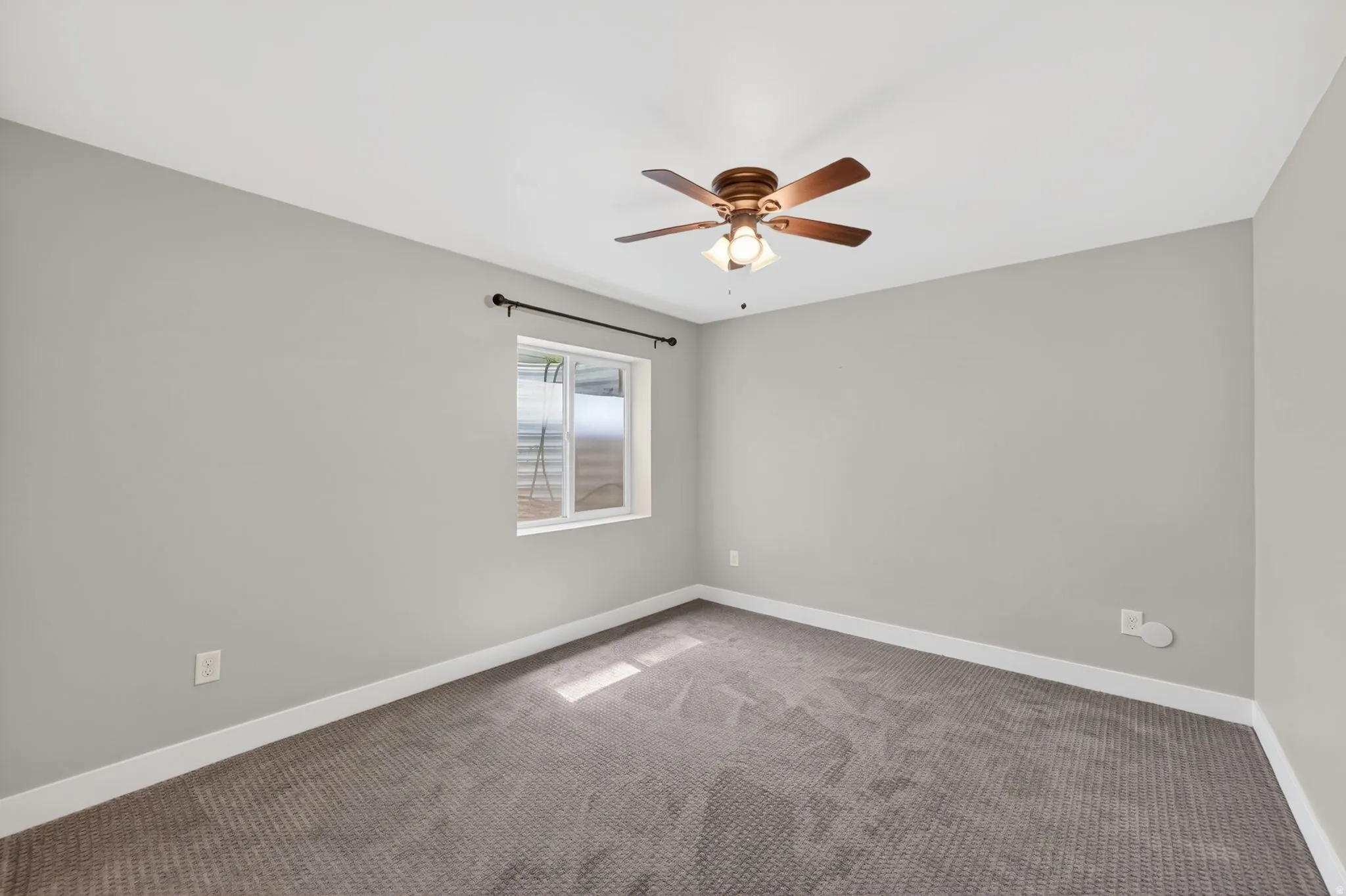 Carpeted room featuring a ceiling fan with light fixture, a window with horizontal blinds, and neutral grey walls