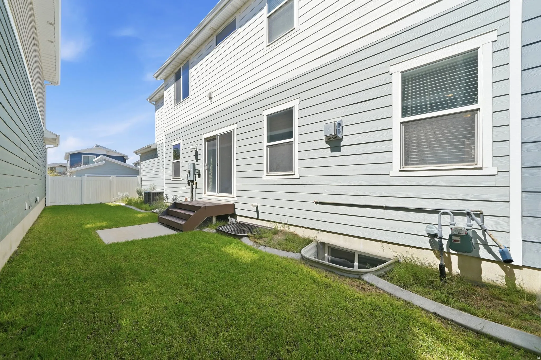 Rear exterior featuring light blue siding, white trim, sliding glass door, a dark wood-finish deck with stairs, and a window well