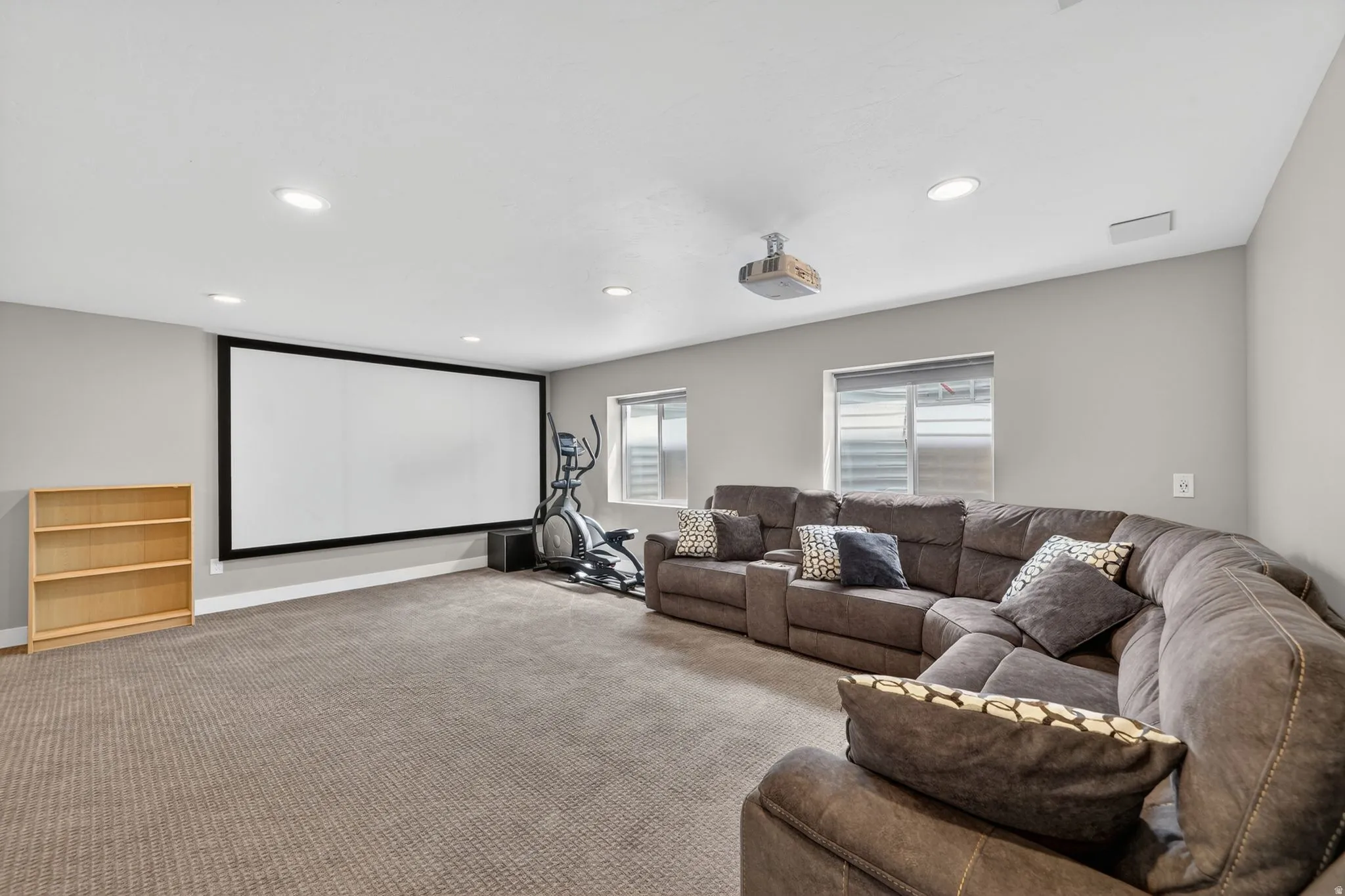 Spacious recreation room featuring a large projection screen, recessed lighting, and soft carpet flooring