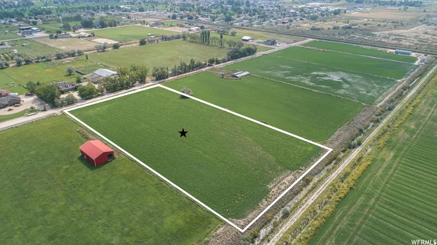 Expansive agricultural land featuring a red barn structure, bordered by a visible irrigation channel