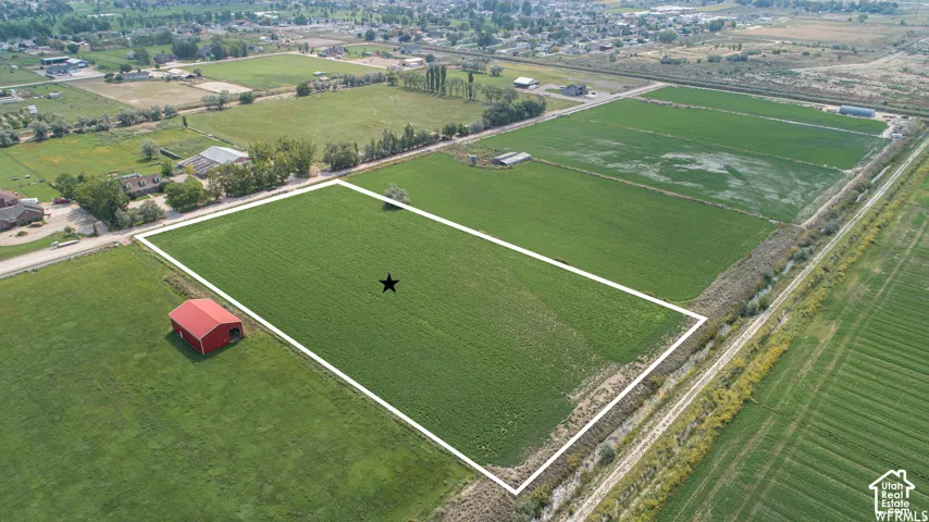 Expansive agricultural land featuring a red barn structure, bordered by a visible irrigation channel