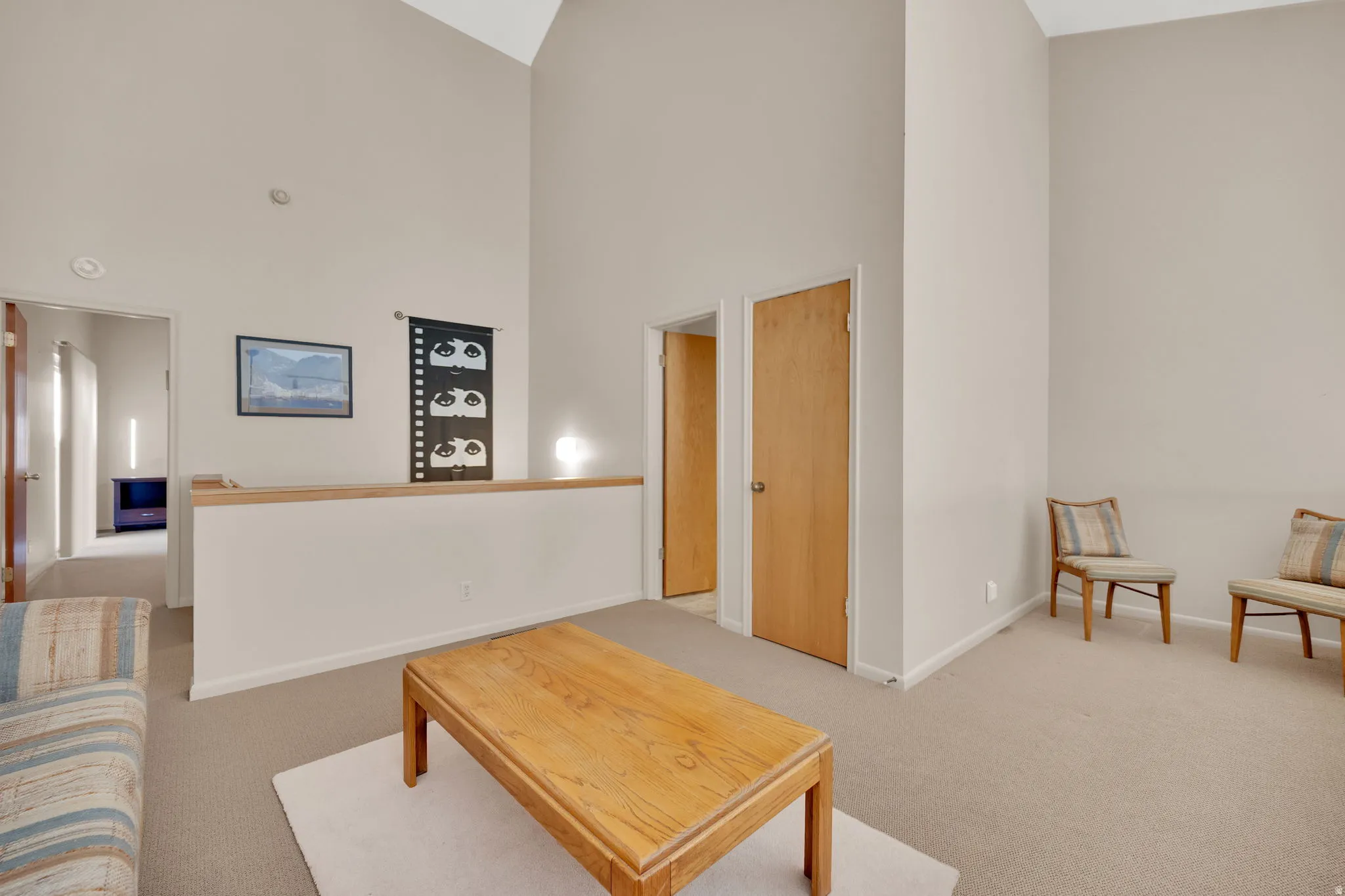 Vaulted ceiling loft space featuring light neutral walls, light-toned carpeting, and wood-finish doors