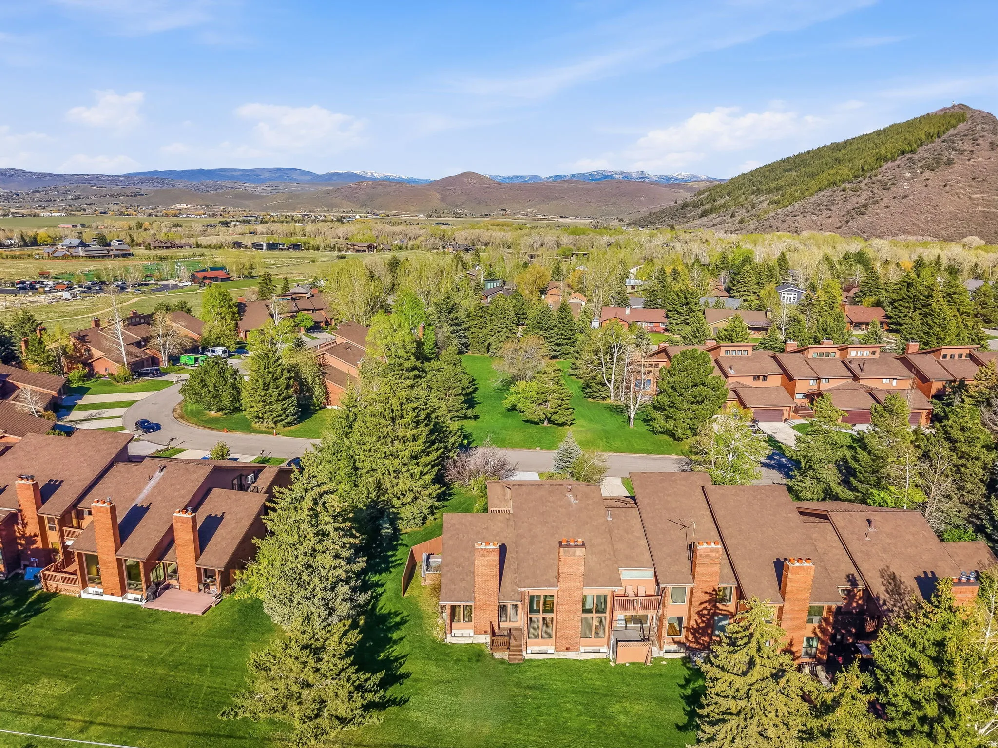Aerial panorama showcasing a community of properties with terracotta-colored roofs and brick exteriors, surrounded by lush green lawns and abundant mature trees
