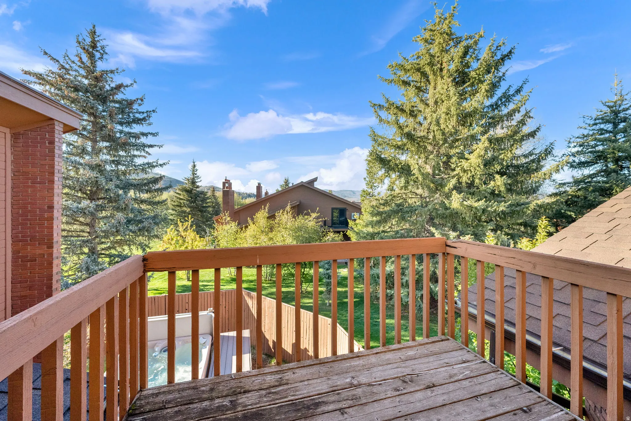 Upper-level wood deck with a slatted railing, offering expansive views of mature evergreen trees and distant mountains