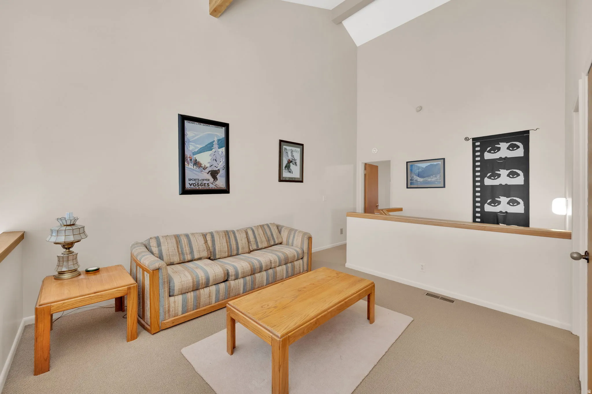 Vaulted ceiling with exposed beam, neutral wall paint, and light-colored carpeting