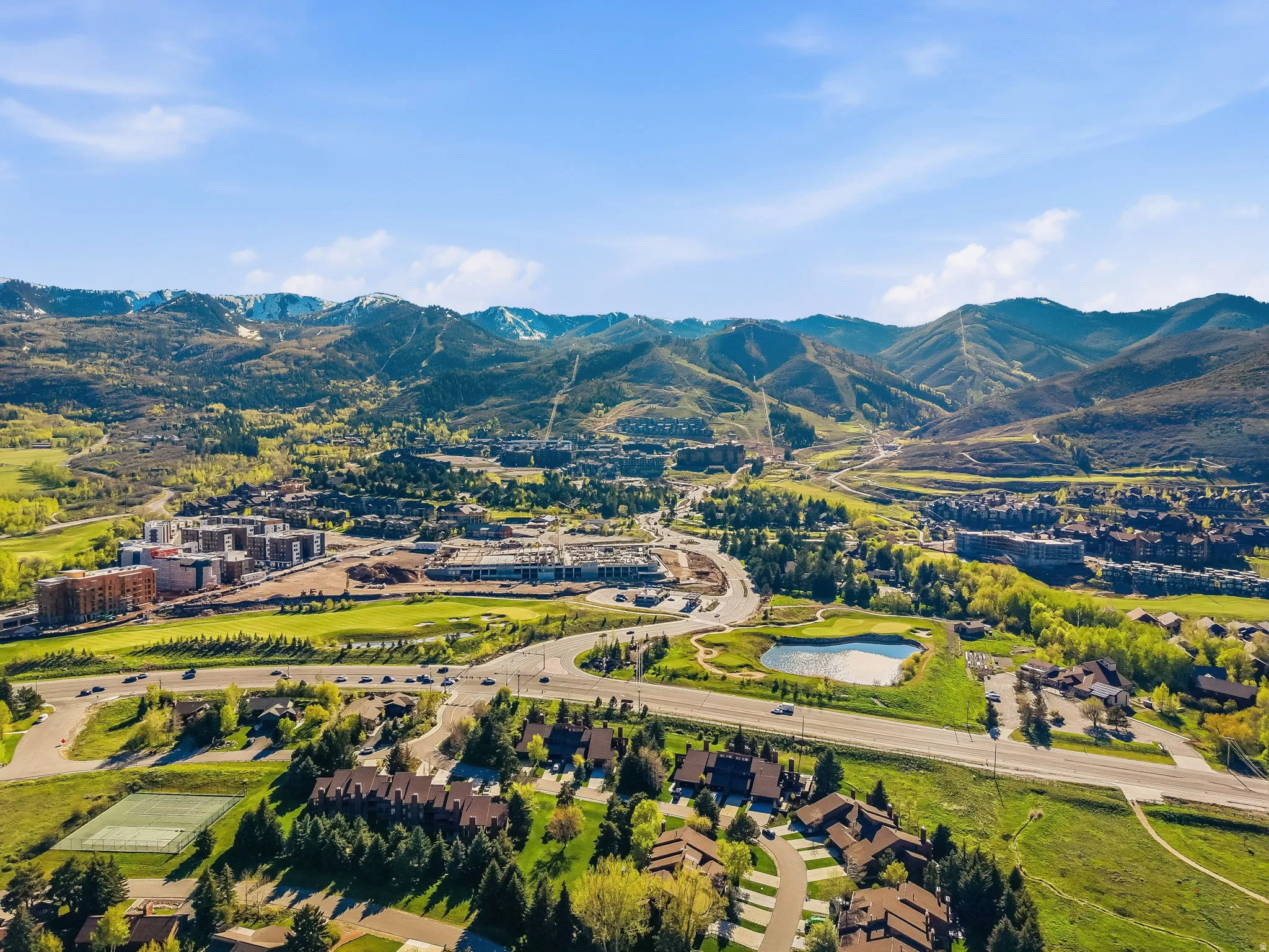 Expansive mountain setting featuring diverse architectural styles, a golf course with a pond, paved roadways, and surrounding natural landscapes