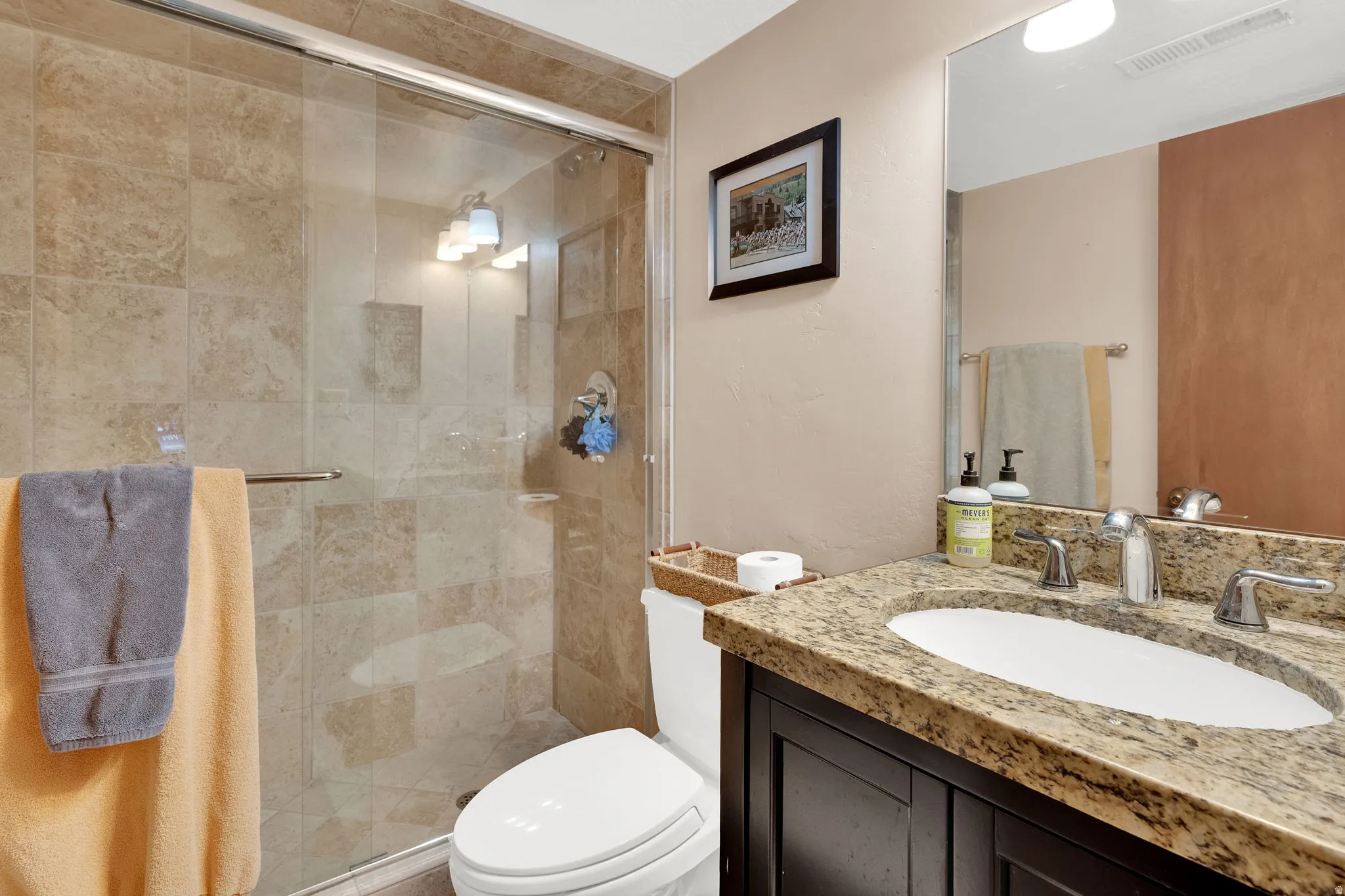 Bathroom featuring a glass-enclosed shower with tile surround, a vanity with a stone-finish countertop, an undermount sink, and a dark wood-finish cabinet
