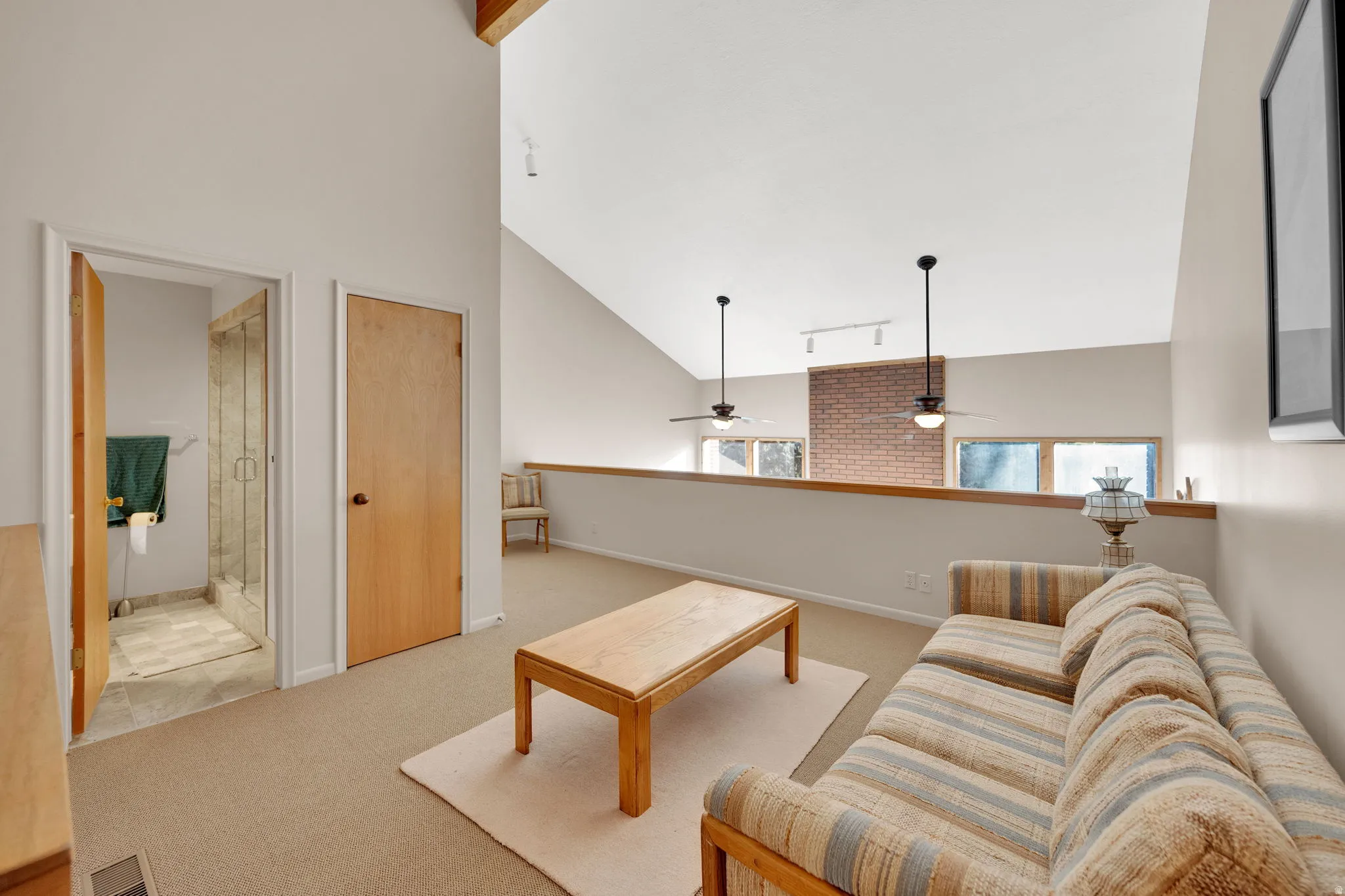Expansive room featuring vaulted ceilings, exposed wood beams, and a partial brick accent wall
