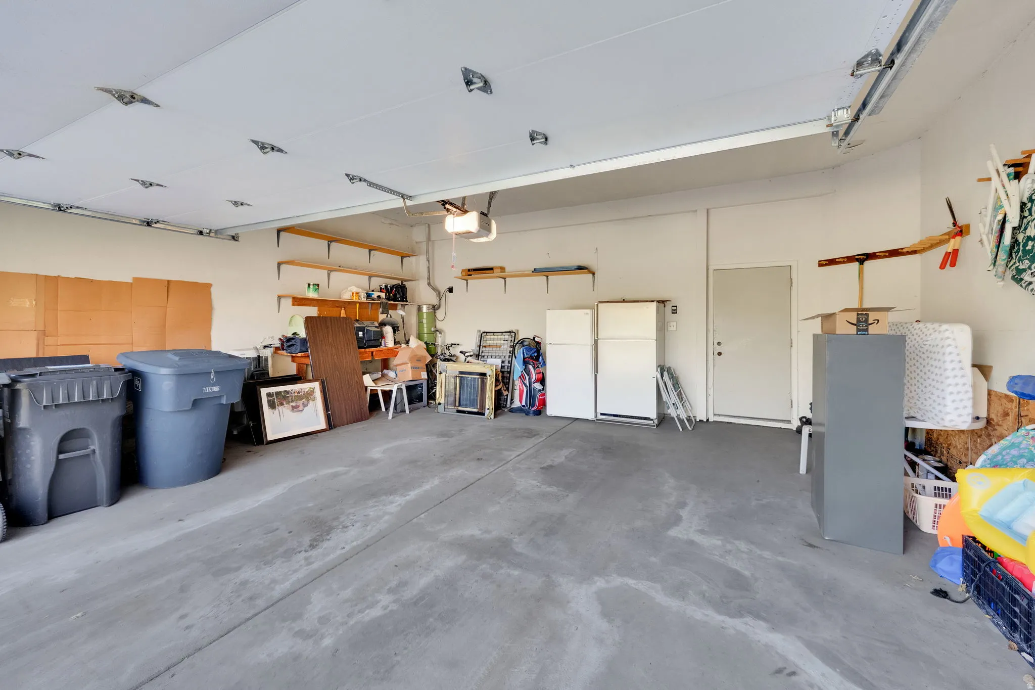 Spacious garage with concrete flooring, overhead garage door rails, a side entry door, and built-in shelving