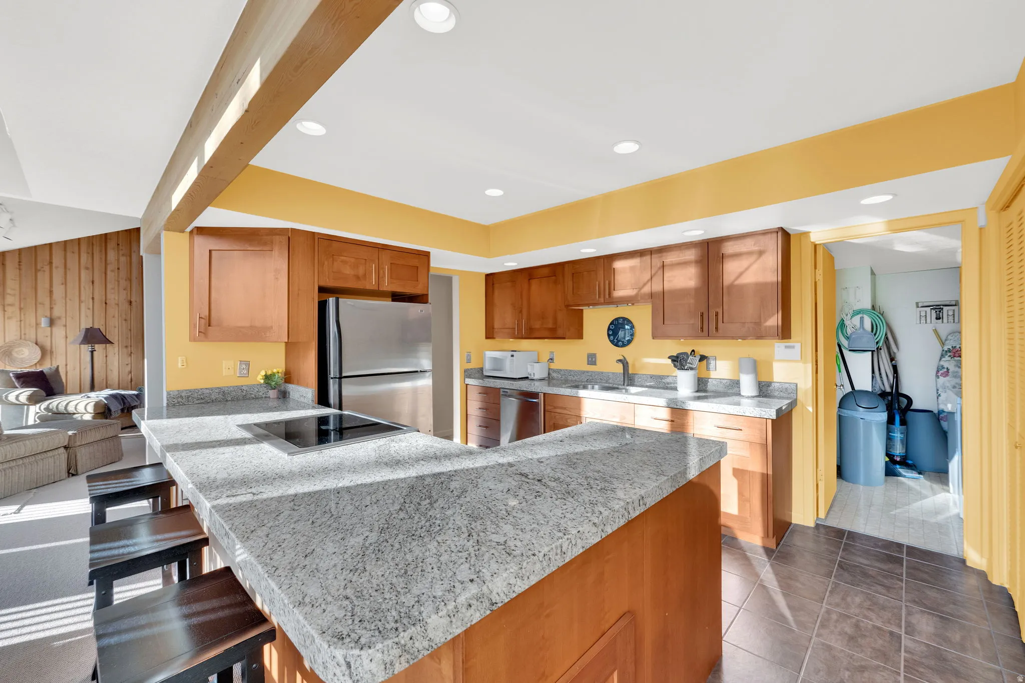 Kitchen featuring an expansive granite-look countertop island with an integrated cooktop, wood cabinetry, and stainless steel appliances