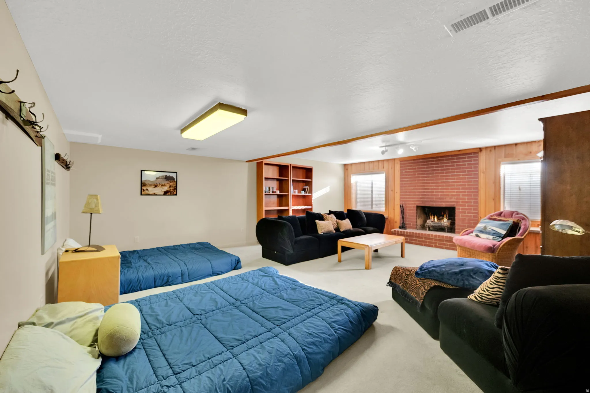 Spacious room featuring a brick fireplace, built-in shelving, wood paneling, and light-colored carpeting