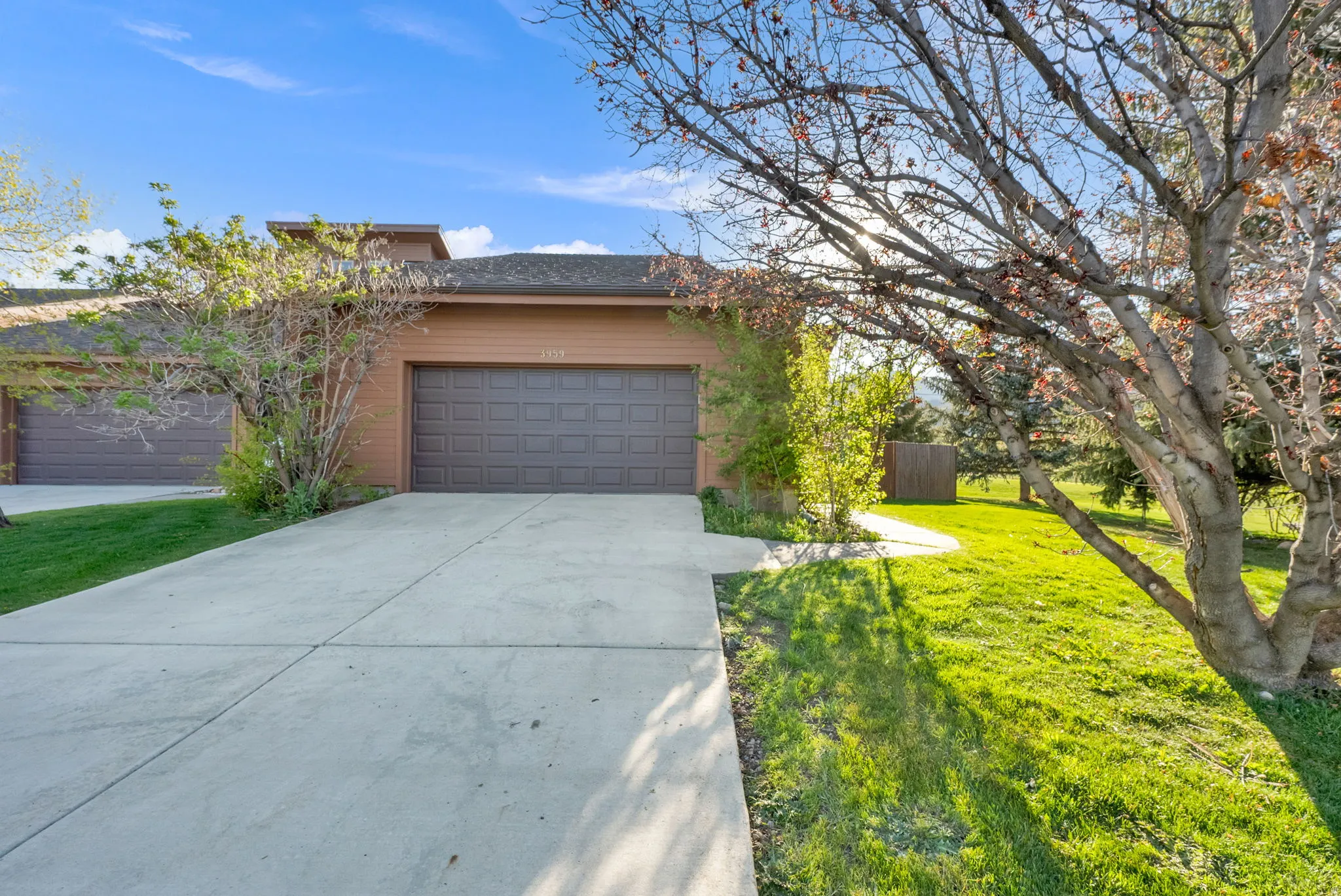 Single-story residence featuring a two-car garage with a paneled door, concrete driveway, and a light brown exterior