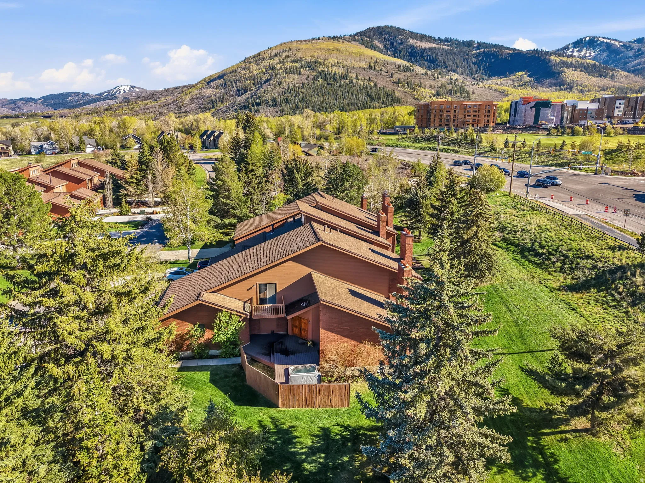 Multi-level brown-sided residence with multiple chimneys, featuring a private deck with a hot tub, surrounded by mature evergreen trees