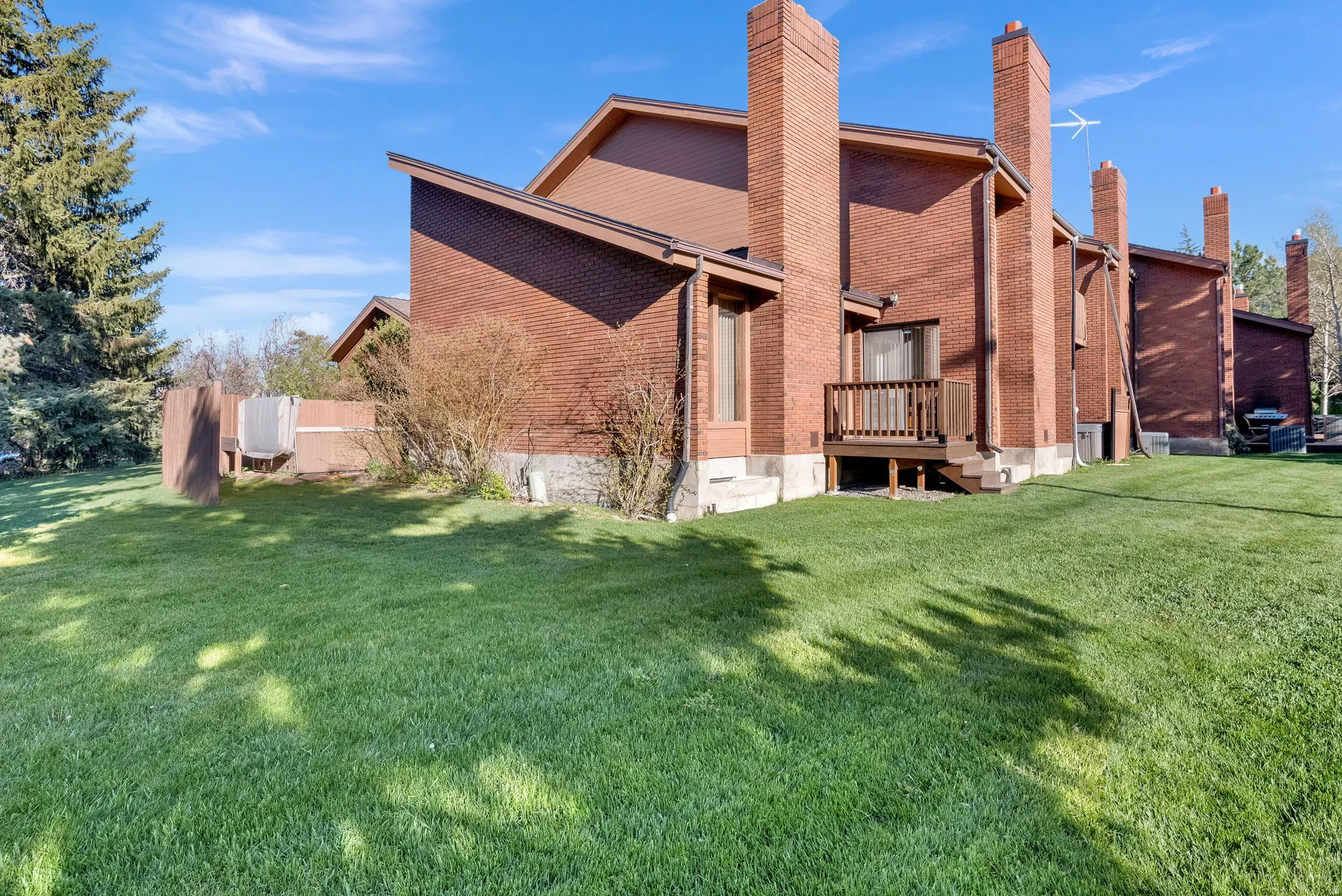 Brick exterior featuring multiple prominent brick chimneys, a sloped roofline, and a wooden deck with railing