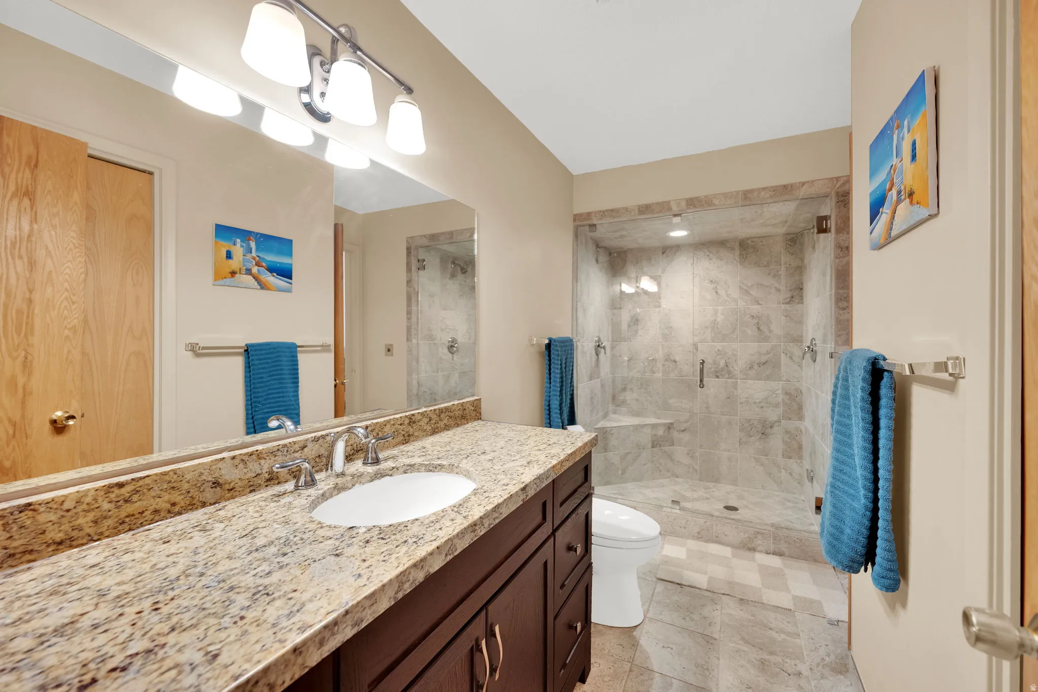 Bathroom featuring a granite countertop vanity with an undermount sink, a large wall-mounted mirror, and a tile-surround walk-in shower with a glass enclosure and built-in bench