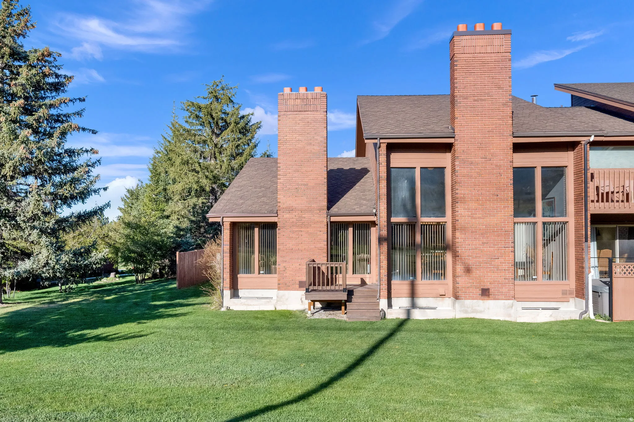 Expansive rear yard featuring a large grass area, mature evergreen trees, and a wooden fence