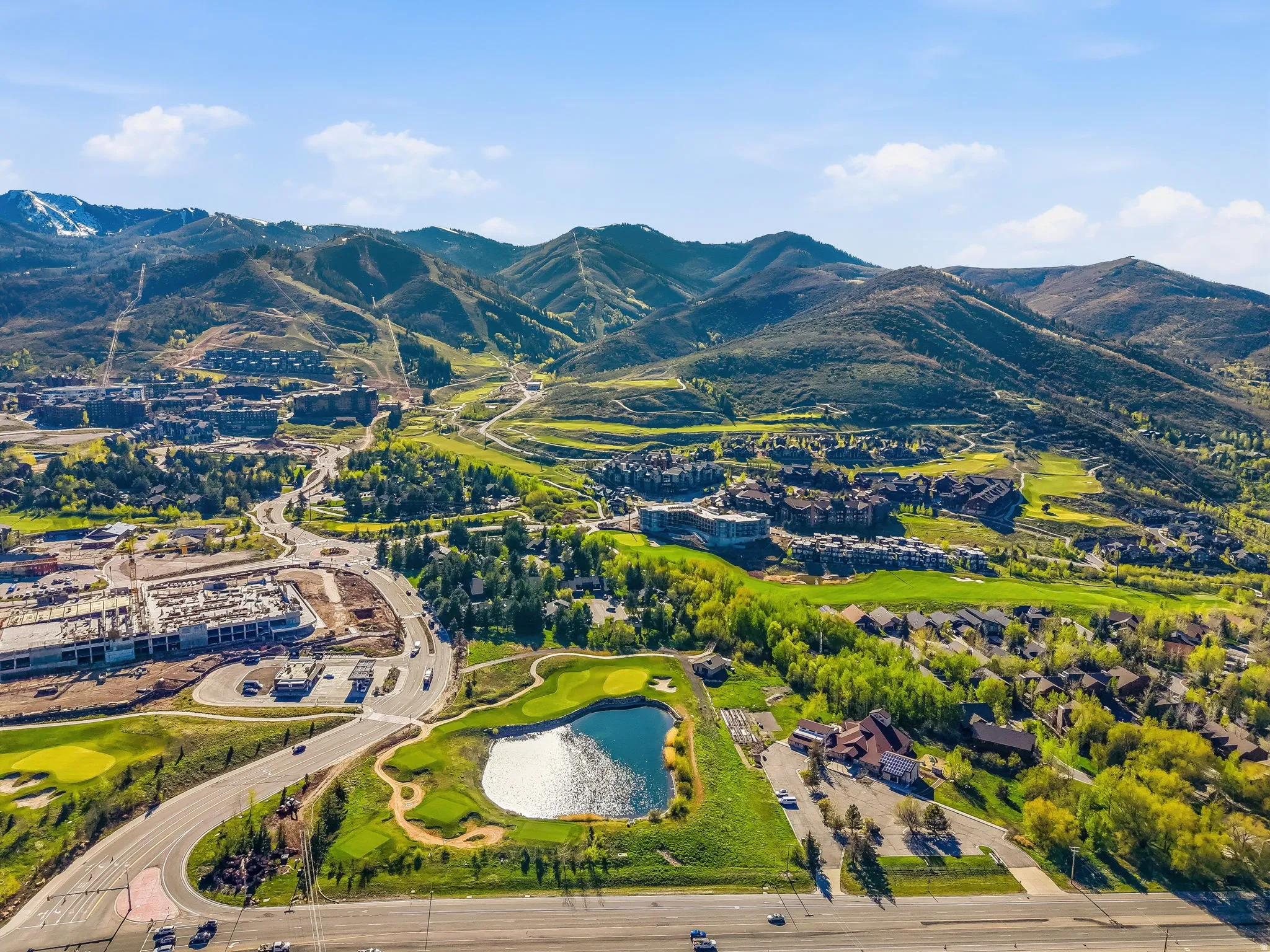 Expansive aerial perspective showcasing a mountainous backdrop, verdant landscapes, and a golf course with a central pond