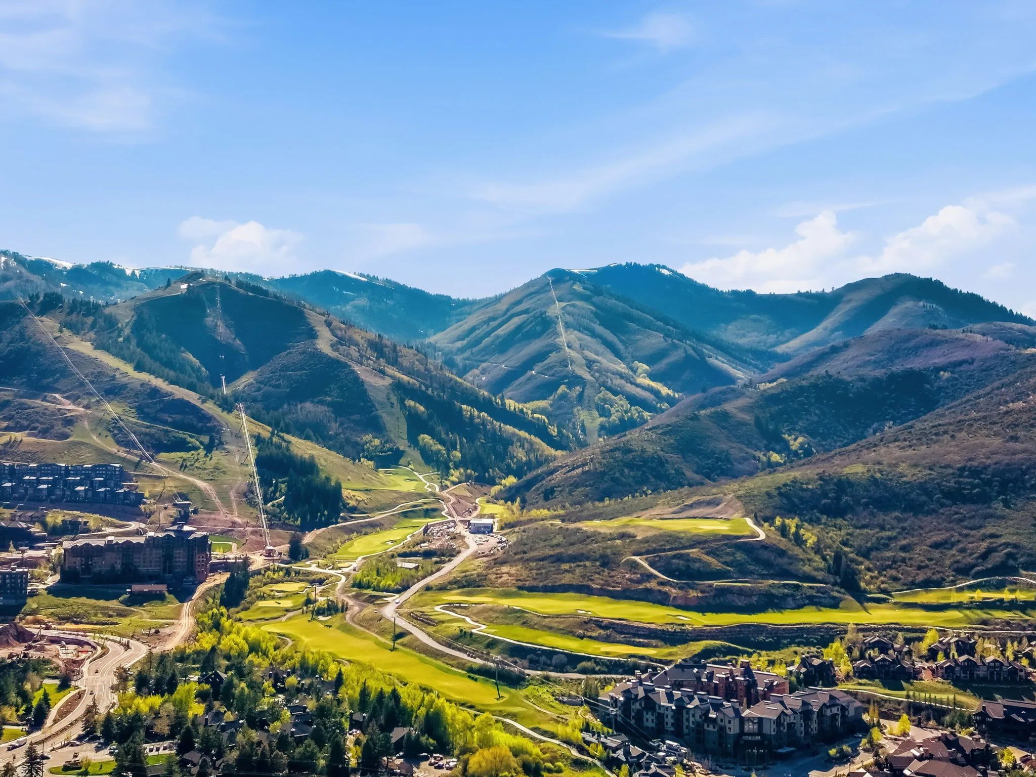 Expansive mountain landscape featuring varied terrain, green golf courses, numerous buildings, and roadways