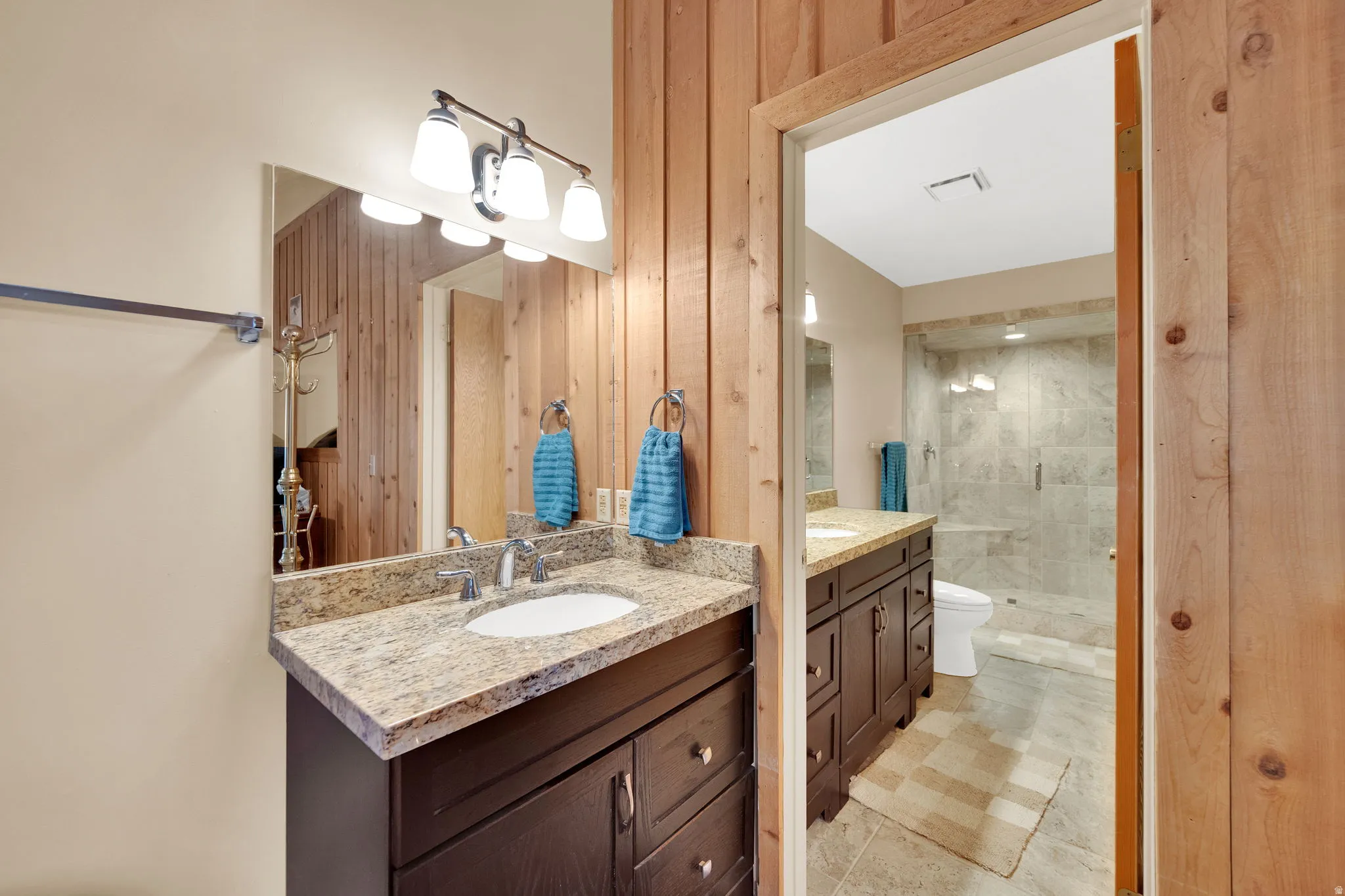 Bathroom featuring wood paneling, a vanity with a granite-style countertop, an undermount sink, and a chrome faucet