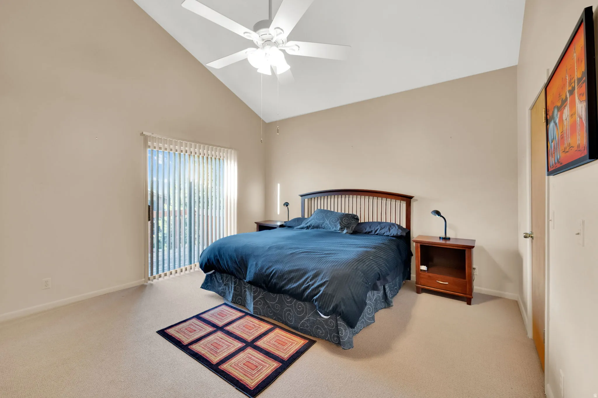 Vaulted ceiling bedroom with a ceiling fan, sliding glass door with vertical blinds, and neutral carpet flooring