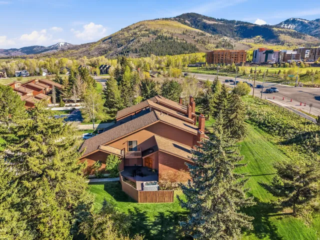 Multi-level brown-sided residence with multiple chimneys, featuring a private deck with a hot tub, surrounded by mature evergreen trees