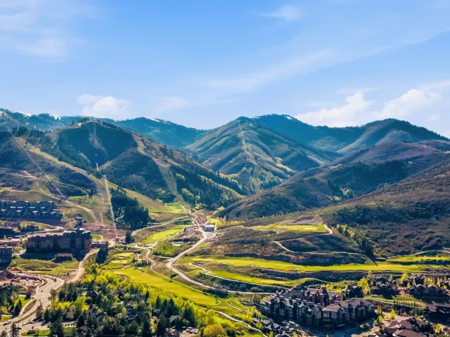 Expansive mountain landscape featuring varied terrain, green golf courses, numerous buildings, and roadways