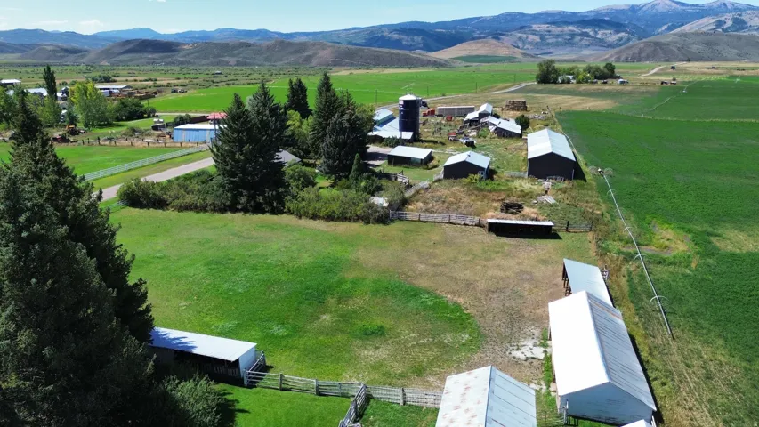 Expansive property featuring multiple outbuildings, fenced enclosures, and distant mountainous terrain