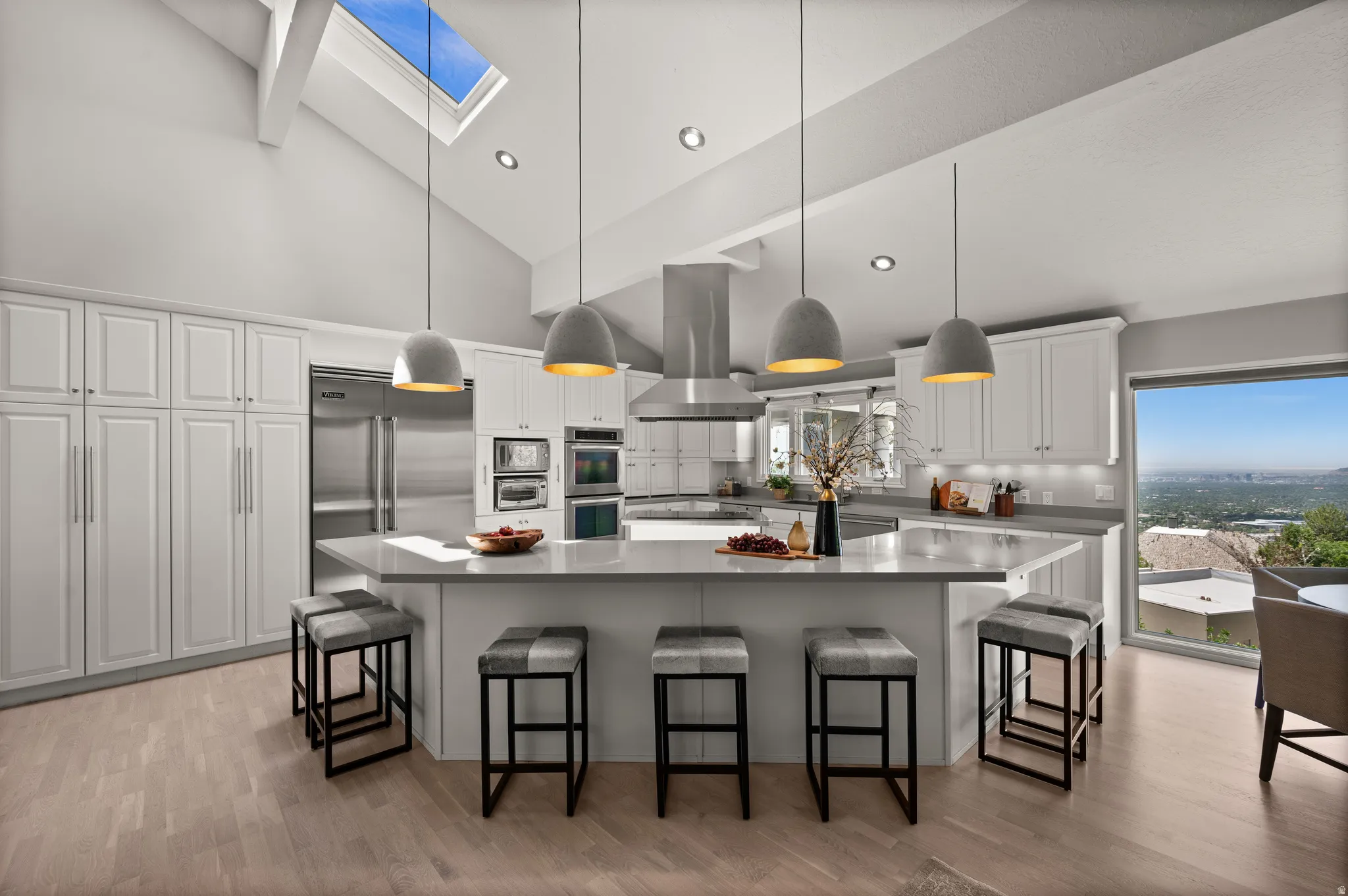 Vaulted ceiling kitchen featuring a skylight, white cabinetry, stainless steel appliances, a center island with pendant lighting, and wood-finish flooring