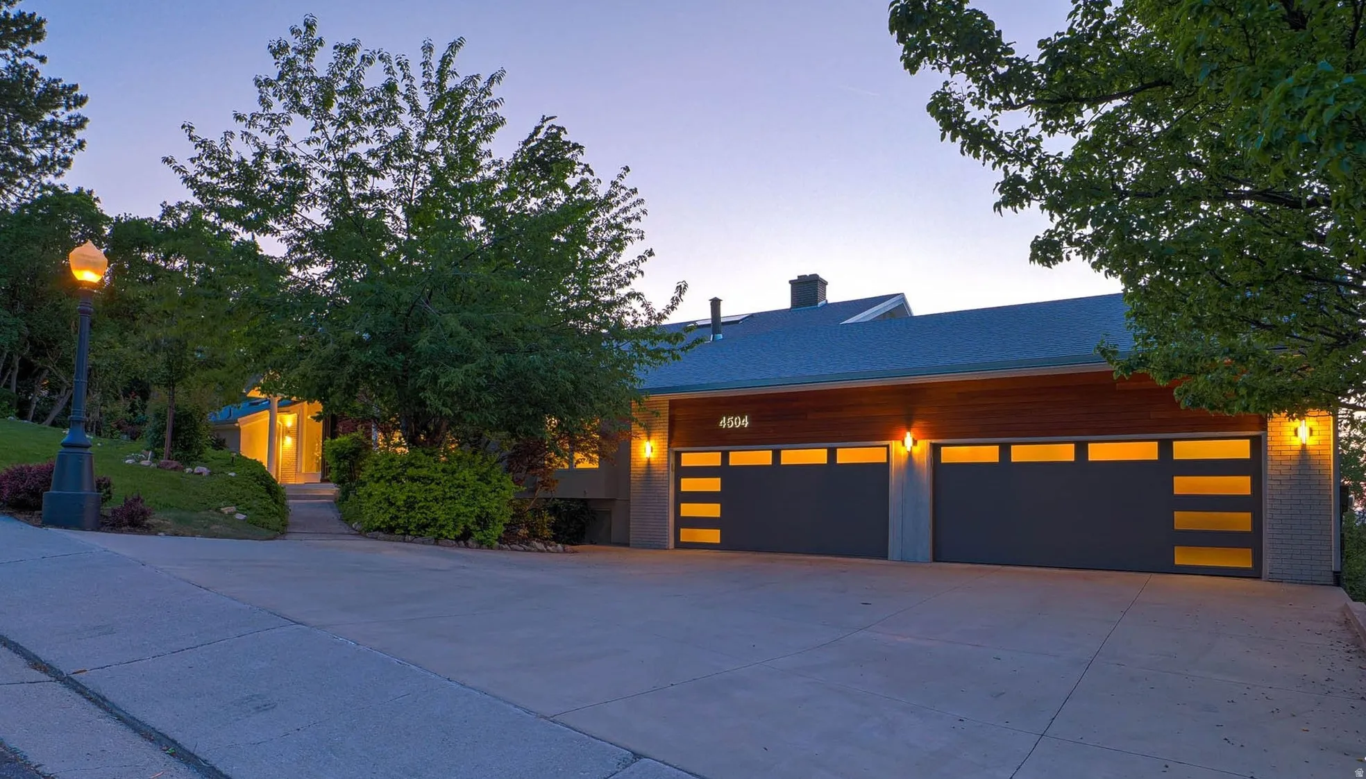 Contemporary exterior featuring two modern garage doors with frosted glass panels, wood-finish siding, and integrated exterior lighting