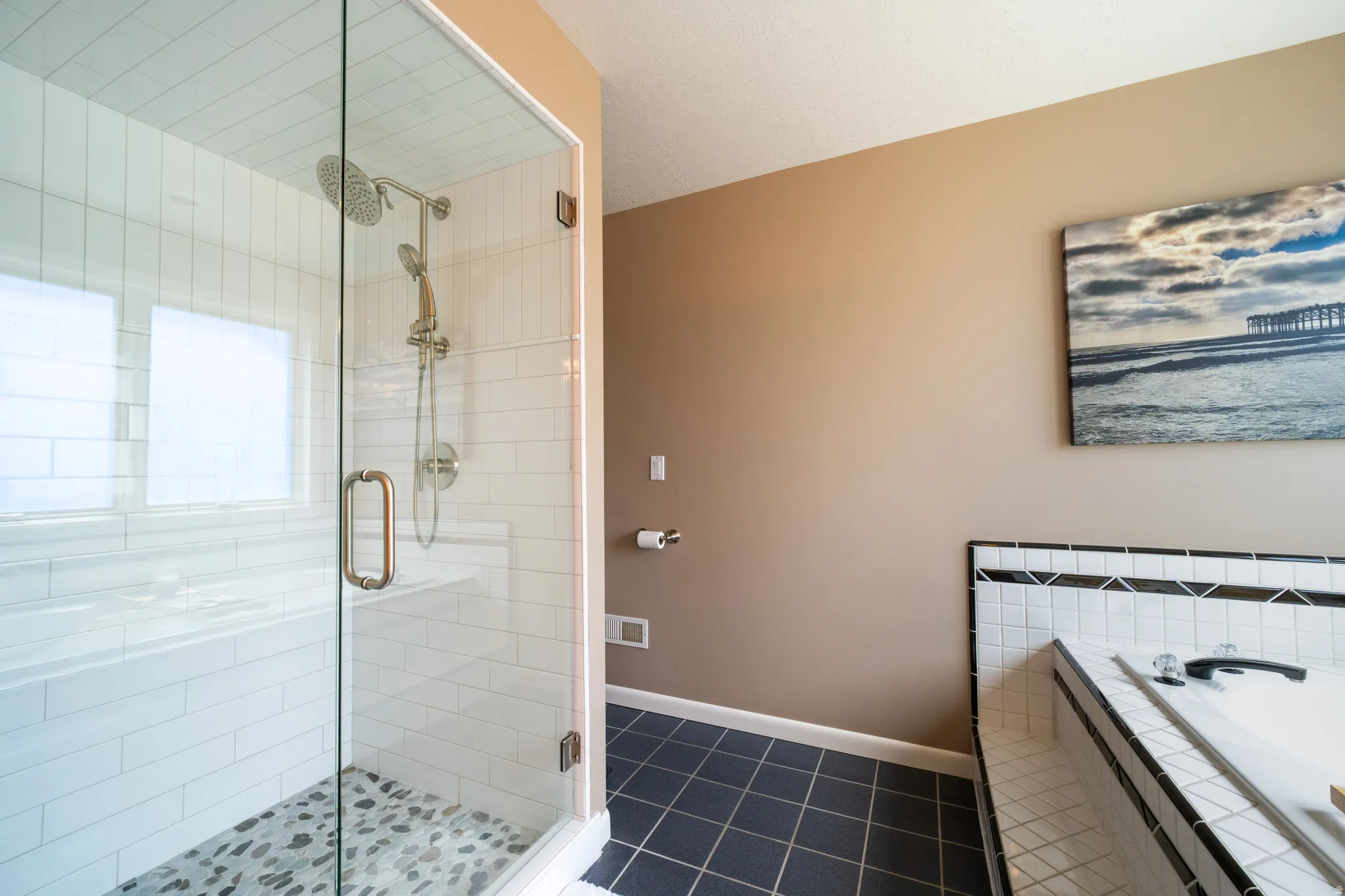 Glass-enclosed shower featuring white subway tile, a multi-function showerhead, and a pebble-tiled floor