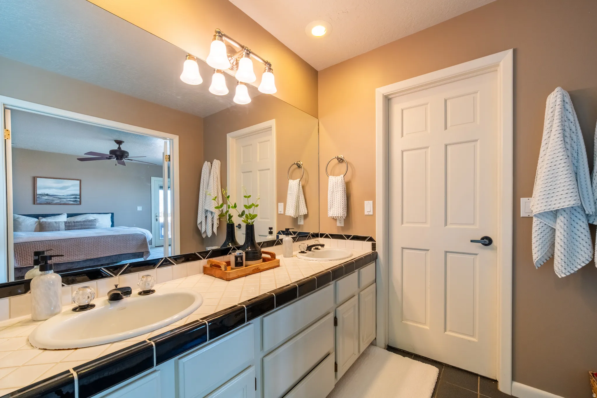 Double vanity featuring oval undermount sinks and white tile countertops with black tile trim